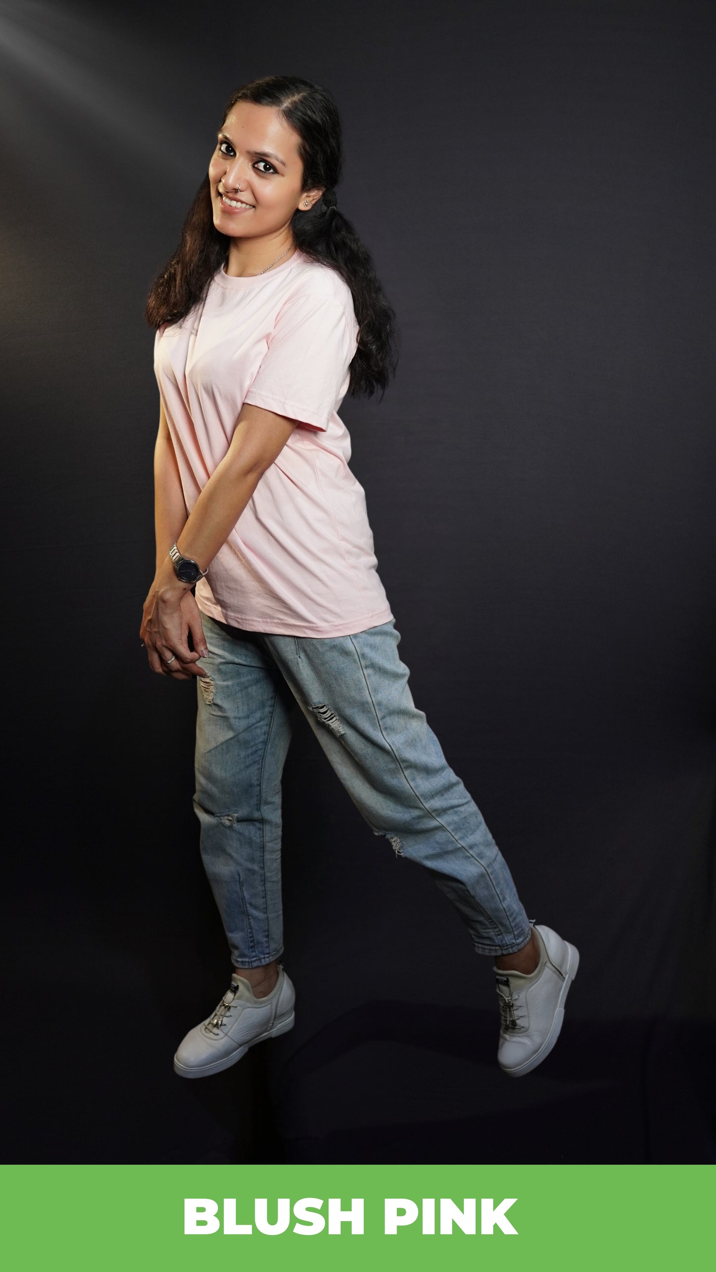 Blush pink round neck women's  t-shirt worn by a brightly smiling woman angled slightly to the side, with one hand grasping the opposite wrist in a casual, relaxed gesture showcasing a loose fit comfortable look-muselot