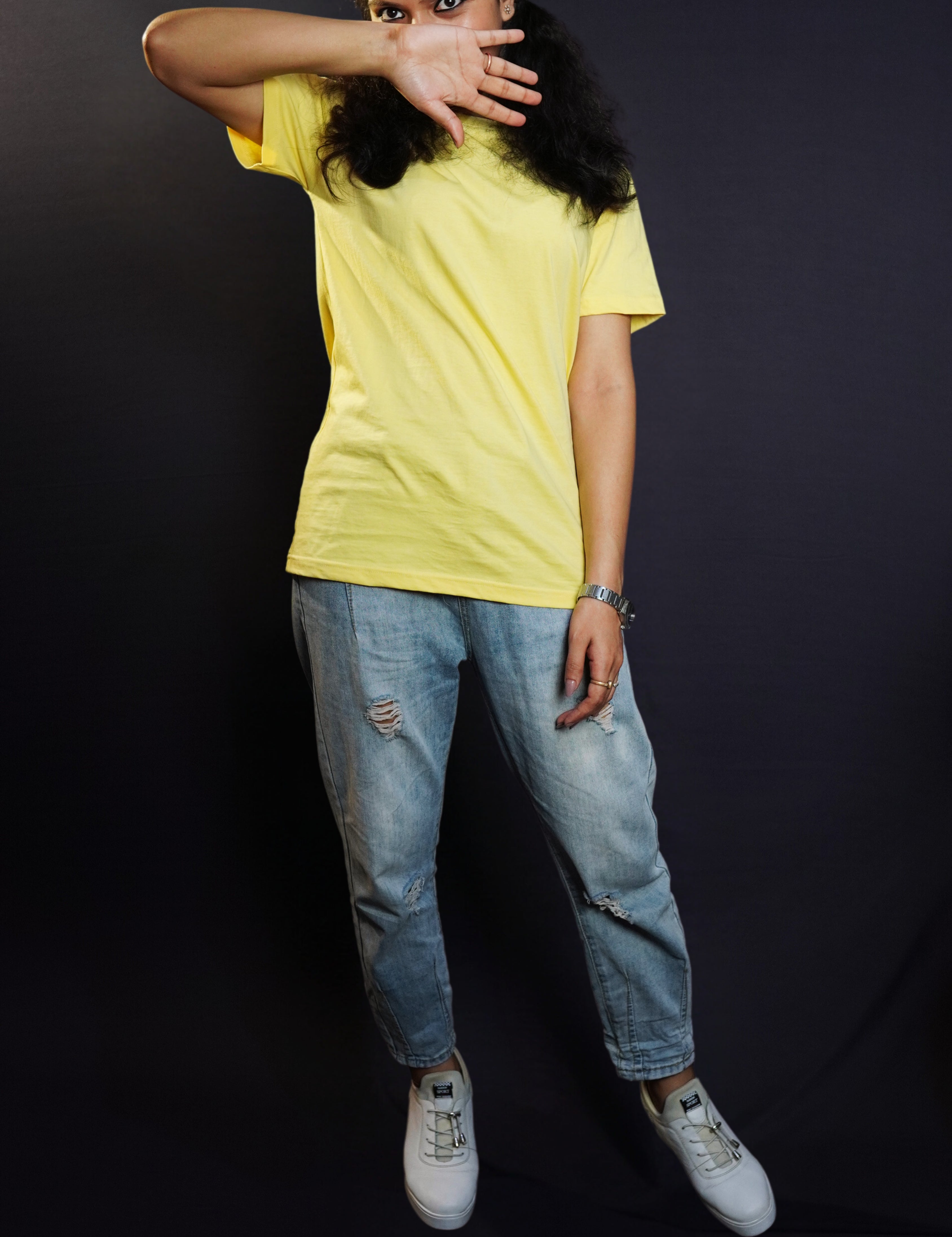A woman wearing a round neck short sleeved long length moisture wicking butter yellow t-shirt, posing with her hand covering half of her face and sparkling eyes looking at the camera, highlighting a casual modern fit-Muselot