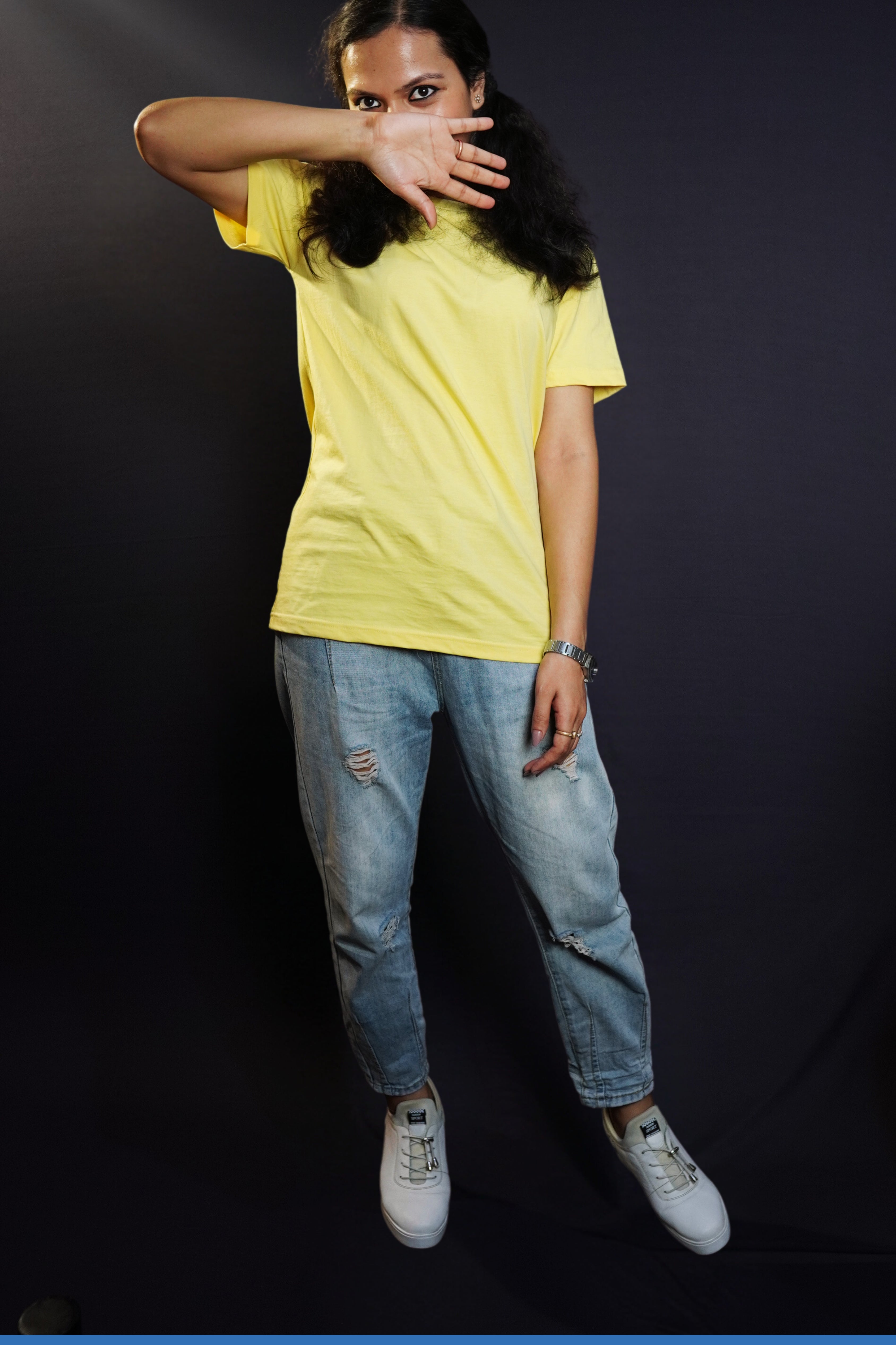 A woman wearing a round neck short sleeved long length moisture wicking butter yellow t-shirt, posing with her hand covering half of her face and sparkling eyes looking at the camera, highlighting a casual modern fit-Muselot
