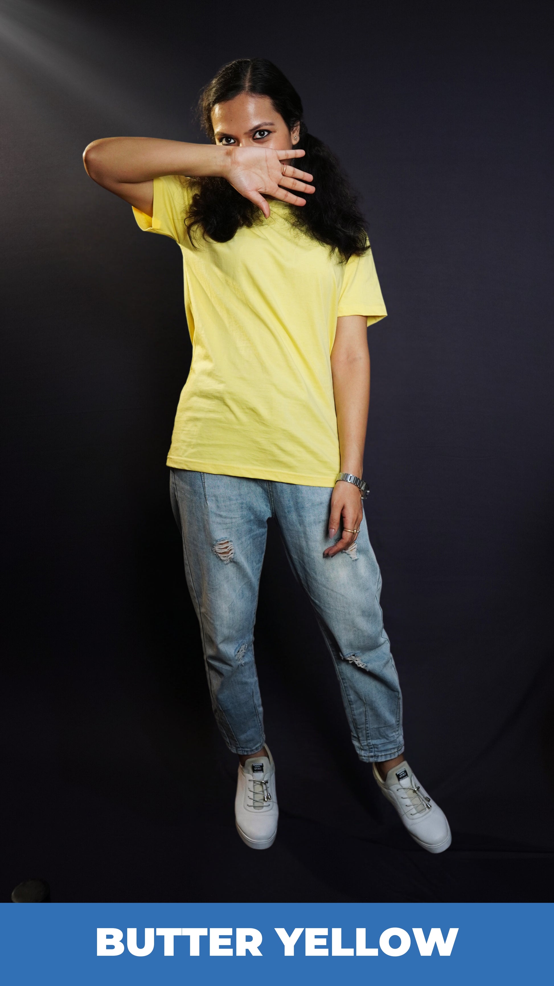 A woman wearing a round neck short sleeved long length moisture wicking butter yellow t-shirt, posing with her hand covering half of her face and sparkling eyes looking at the camera, highlighting a casual modern fit-Muselot