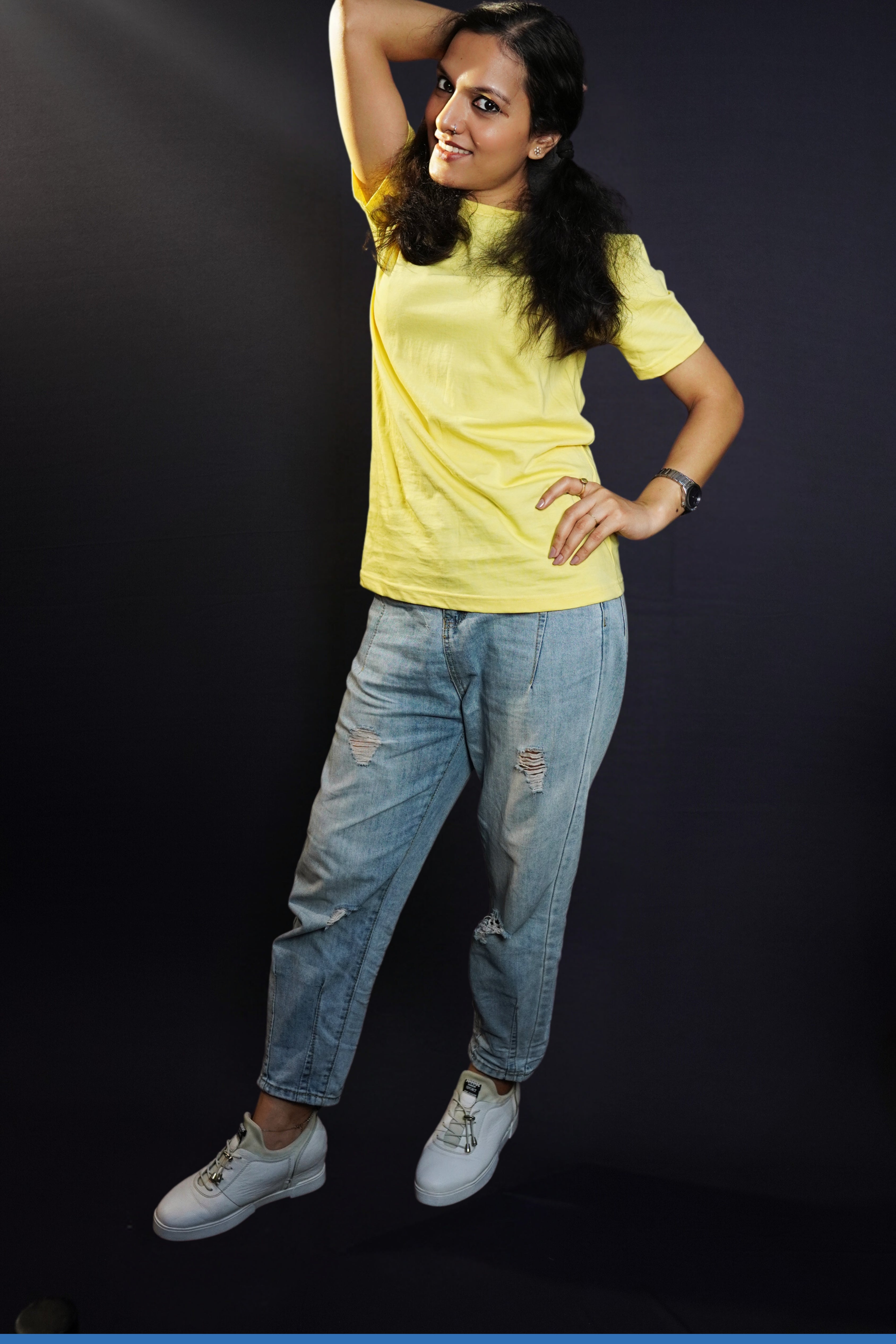 A woman wearing a plain cotton summer butter yellow t-shirt, posing with her hand on her waist and another behind the back of her head, showcasing a trendy voguish look-Muselot
