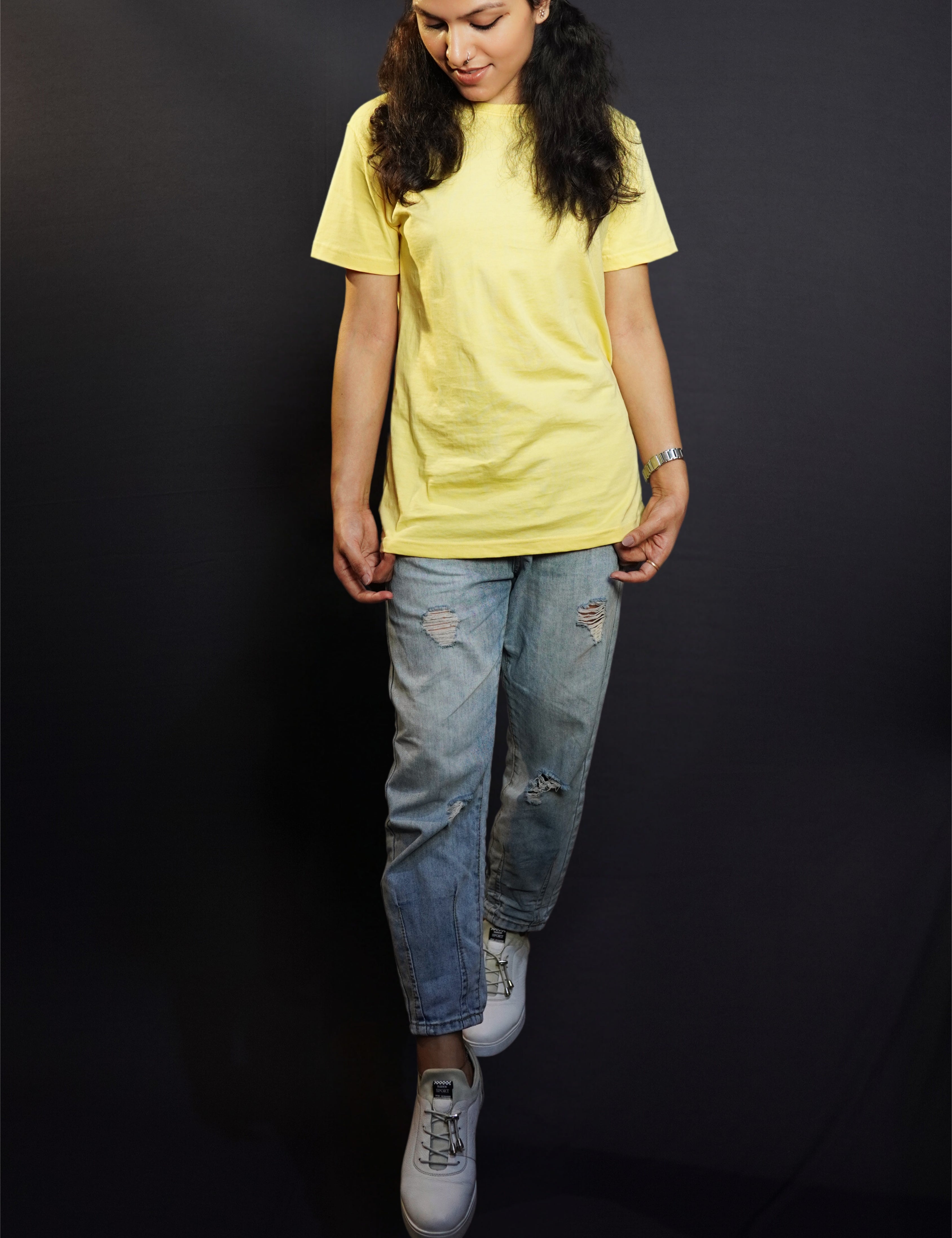 a stylish model wearing a butter yellow plain stretchable t-shirt, standing with her head slightly bent down and her hands grabbing the side of the t-shirt, showcasing an elegant casual fit-Muselot