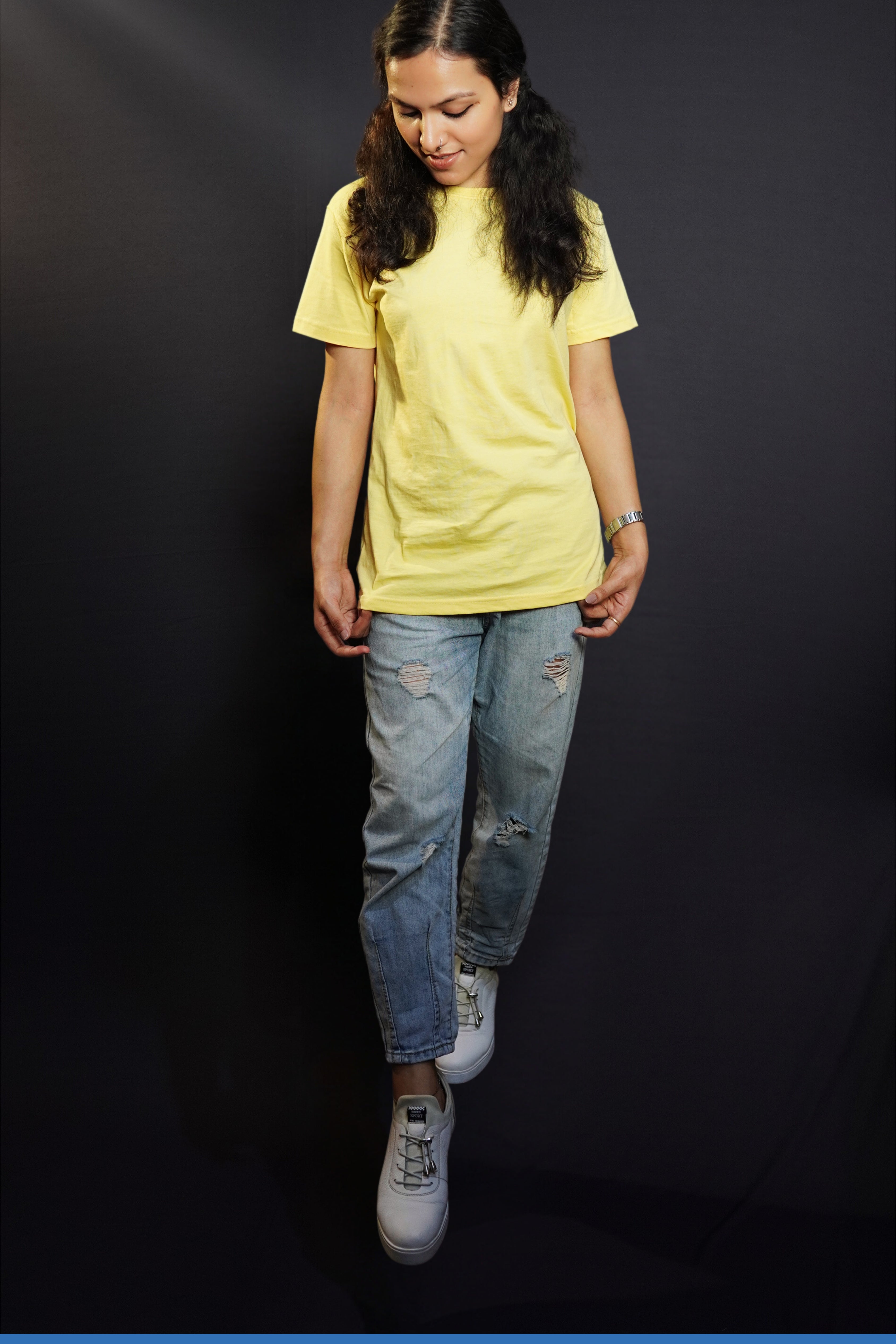 a stylish model wearing a butter yellow plain stretchable t-shirt, standing with her head slightly bent down and her hands grabbing the side of the t-shirt, showcasing an elegant casual fit-Muselot