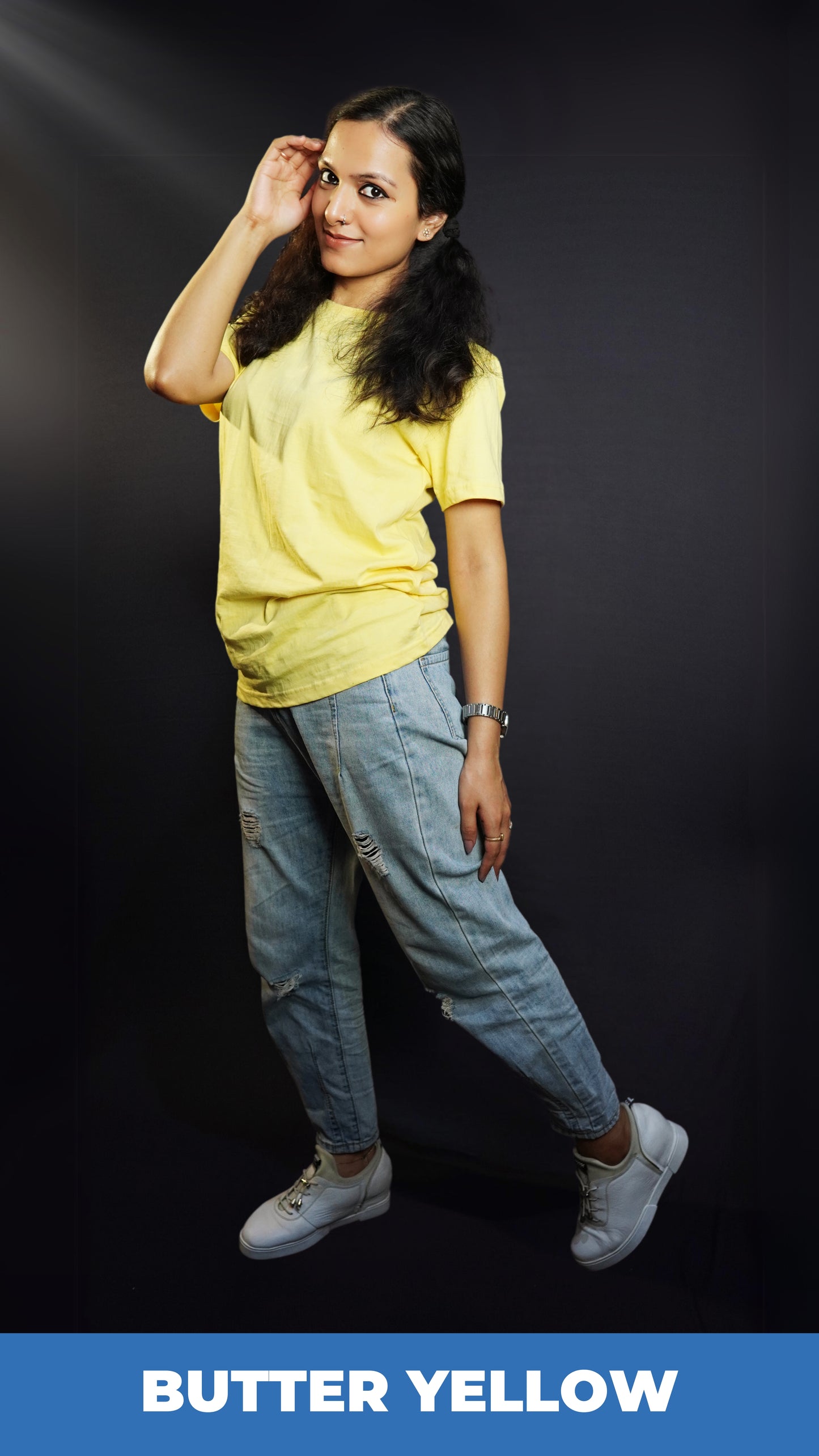 A woman wearing a butter yellow unisex quick drying t shirt, posing with her hand at the side of her head as she stands sideways, showcasing a stylish modern look-Muselot