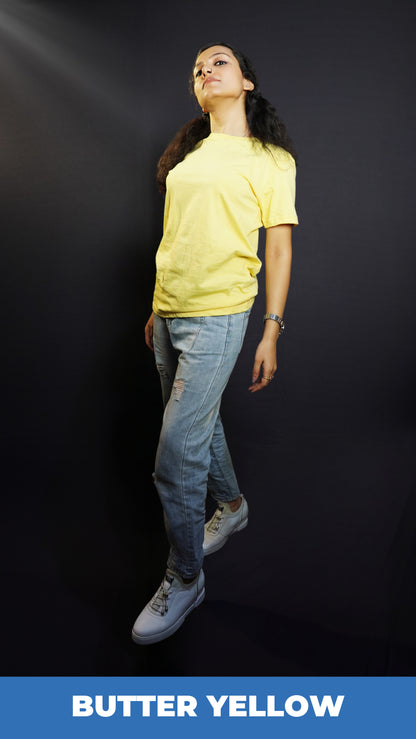 A woman posing as she slightly bends backward with her one leg in front of another, wearing a plain cotton women's round neck butter yellow t-shirt, highlighting a relaxed swank style-Muselot