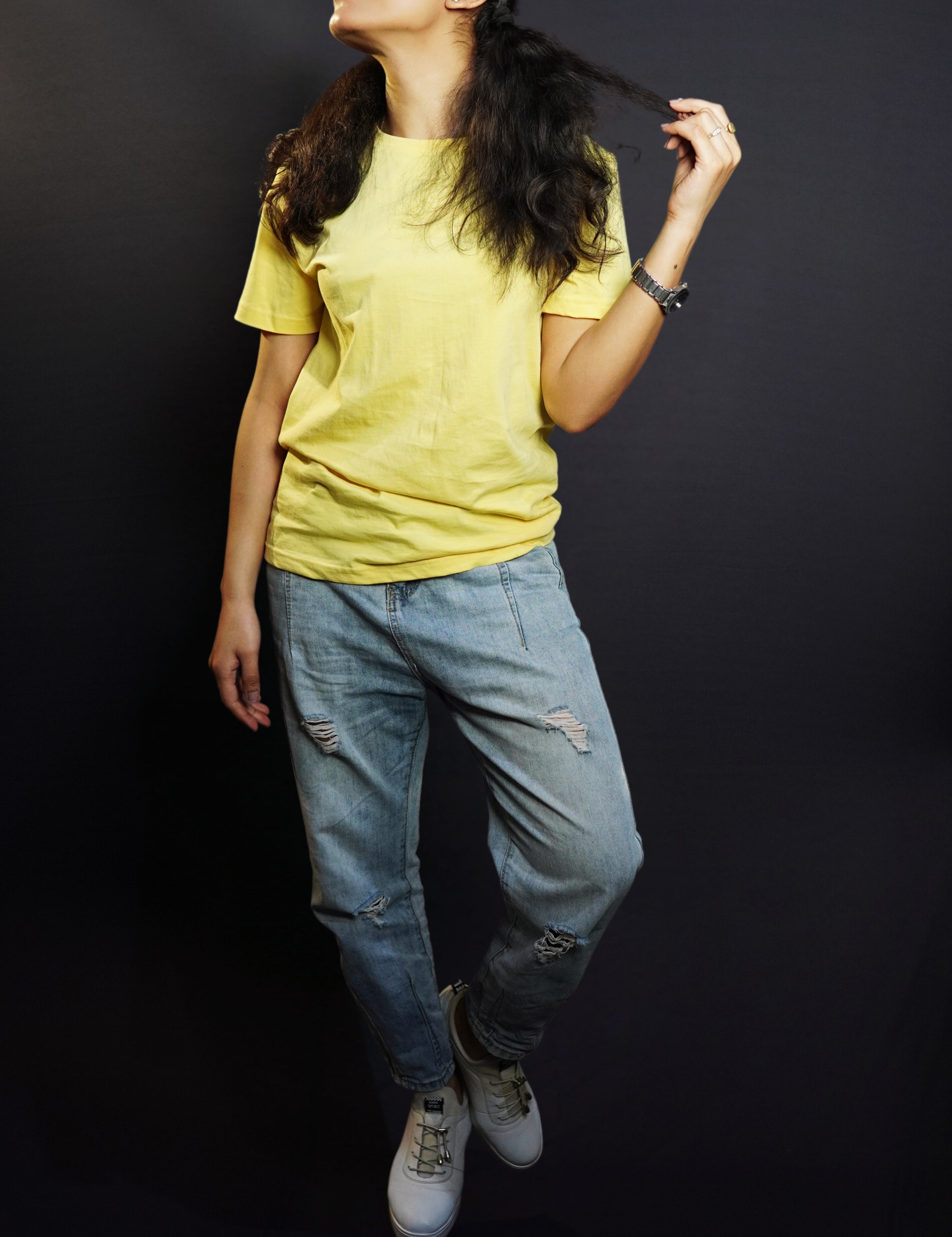 A woman wearing a butter yellow men's round neck long length t-shirt, posing with her hand pulling the tip of her hair as she looks sideways, showcasing an up to the minute baggy fit-Muselot