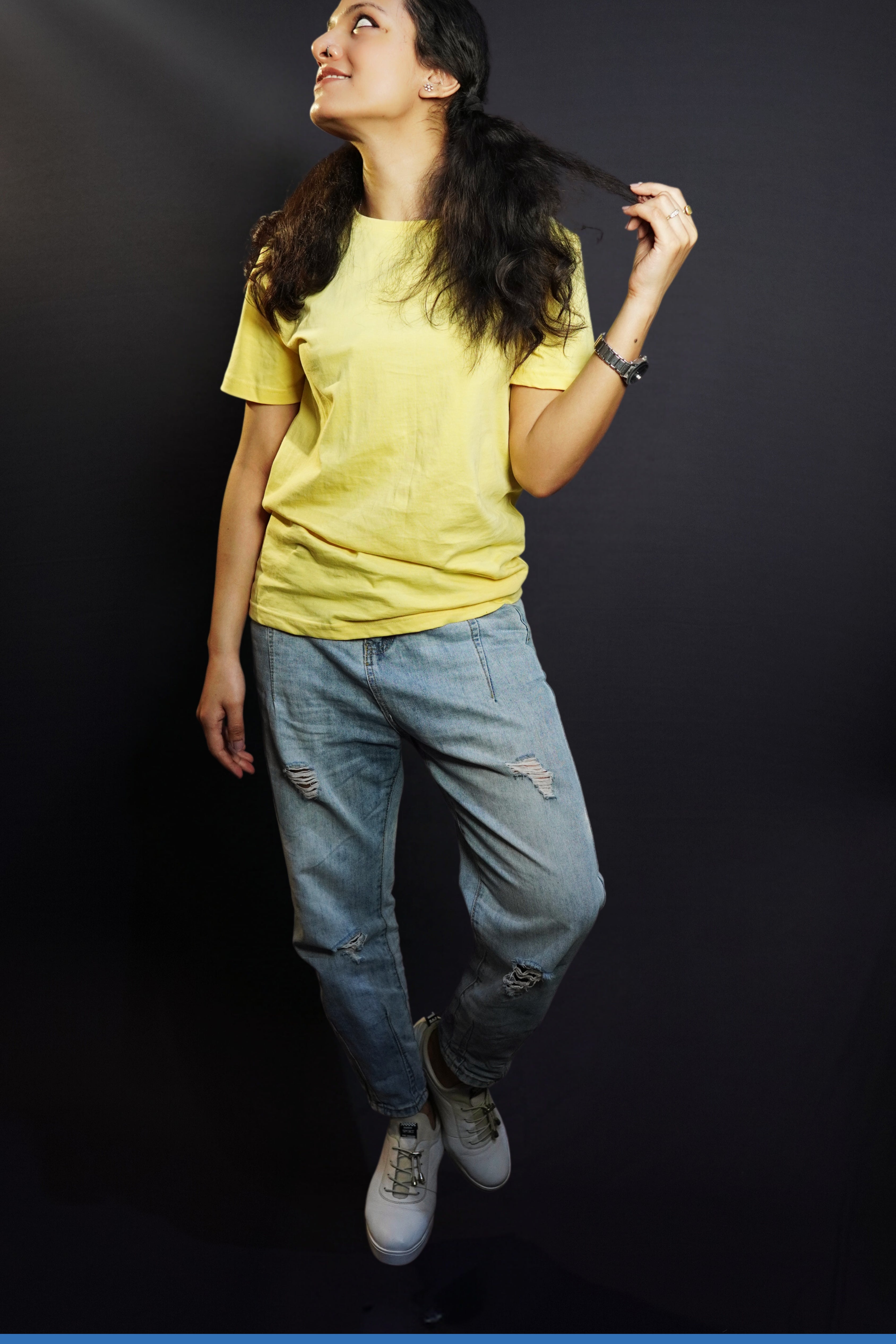 A woman wearing a butter yellow men's round neck long length t-shirt, posing with her hand pulling the tip of her hair as she looks sideways, showcasing an up to the minute baggy fit-Muselot
