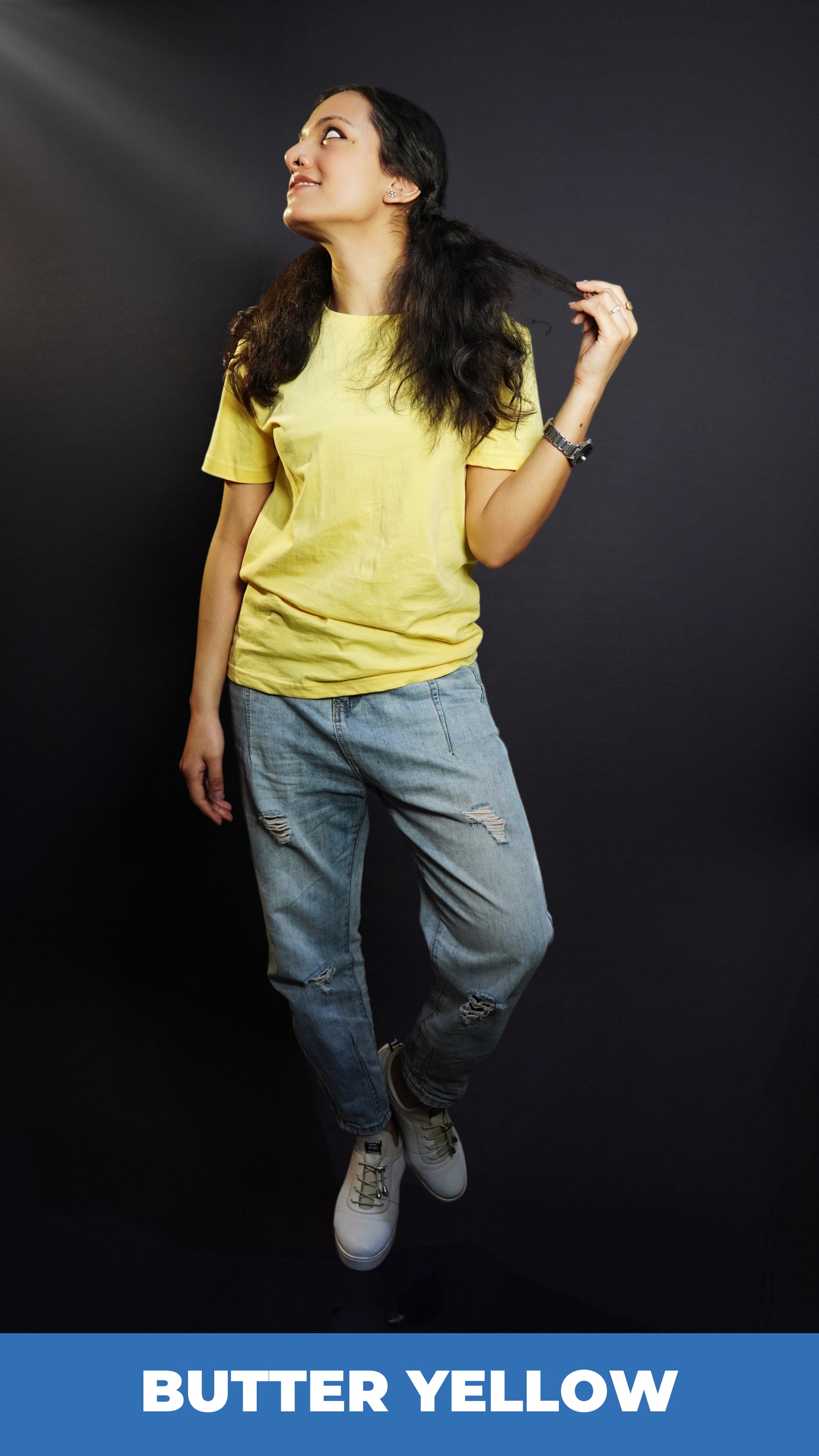 A woman wearing a butter yellow men's round neck long length t-shirt, posing with her hand pulling the tip of her hair as she looks sideways, showcasing an up to the minute baggy fit-Muselot