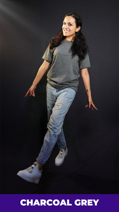 a happy woman walking wearing a charcoal grey t shirt with ripped jeans and white sports shoes with a smile on her face against a dark background-muselot