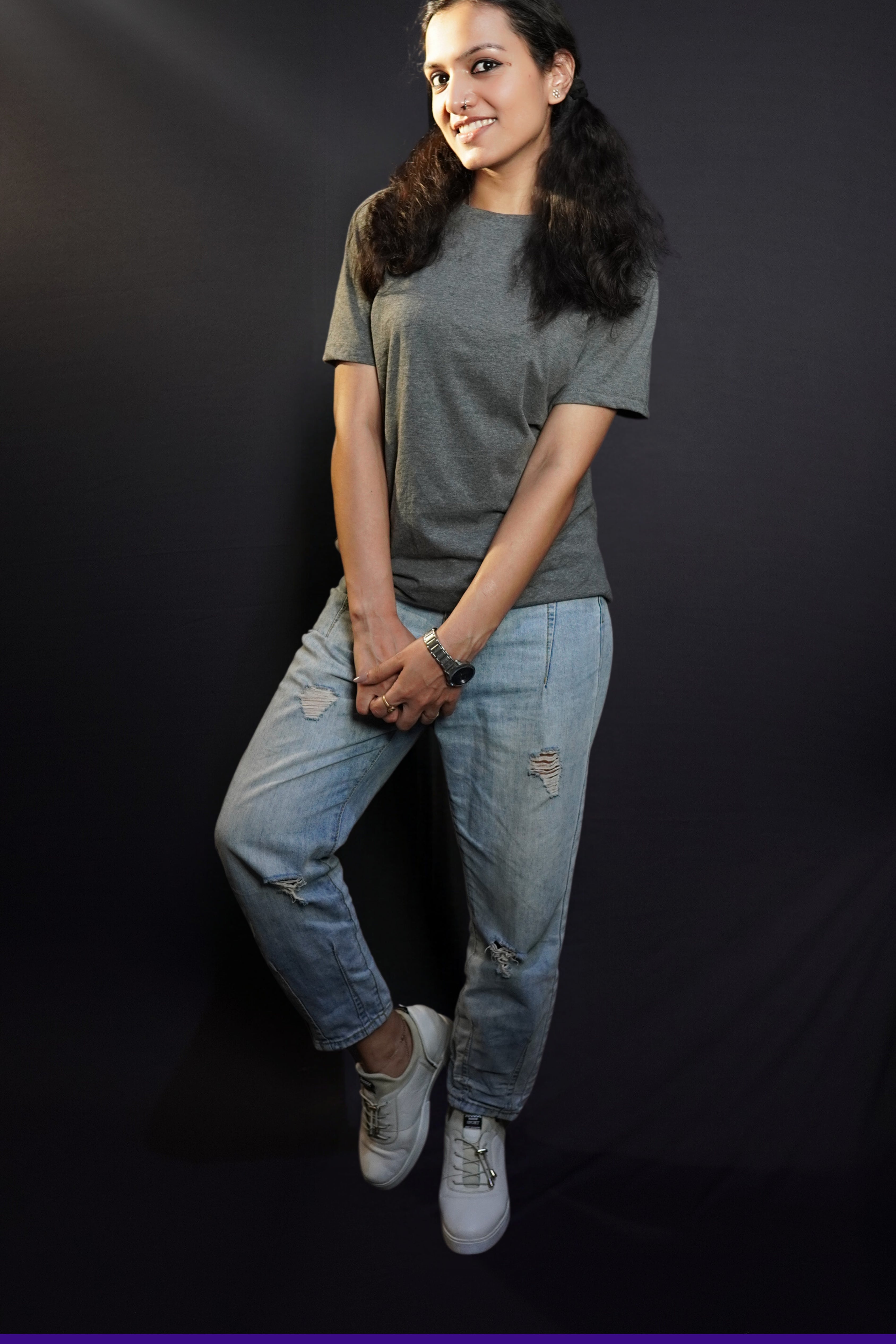 a woman with a smile on her face wearing long length t shirt pairing with ripped jeans and white shoes and a silver watch around her wrist-muselot