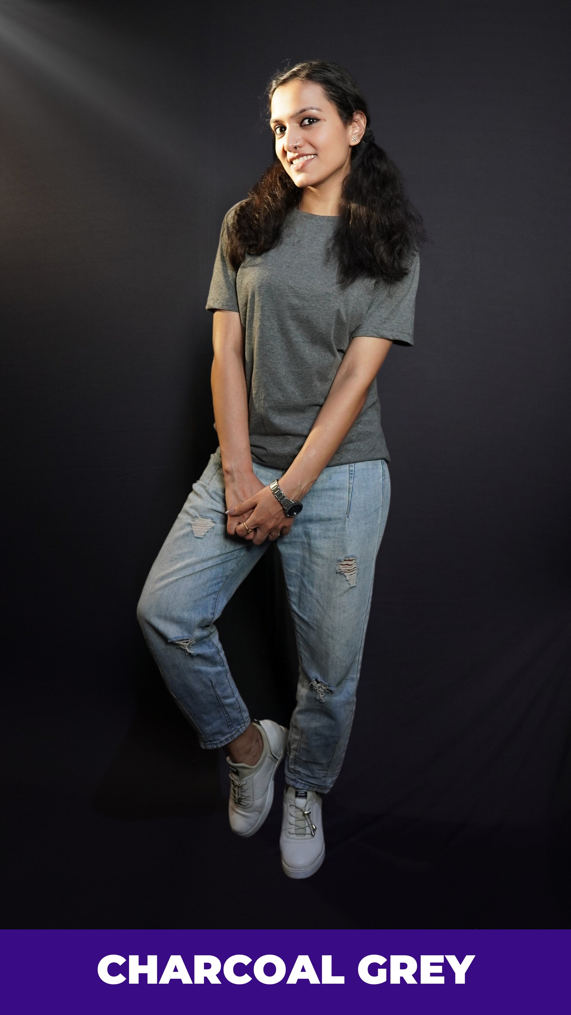 a woman with a smile on her face wearing long length t shirt pairing with ripped jeans and white shoes and a silver watch around her wrist-muselot