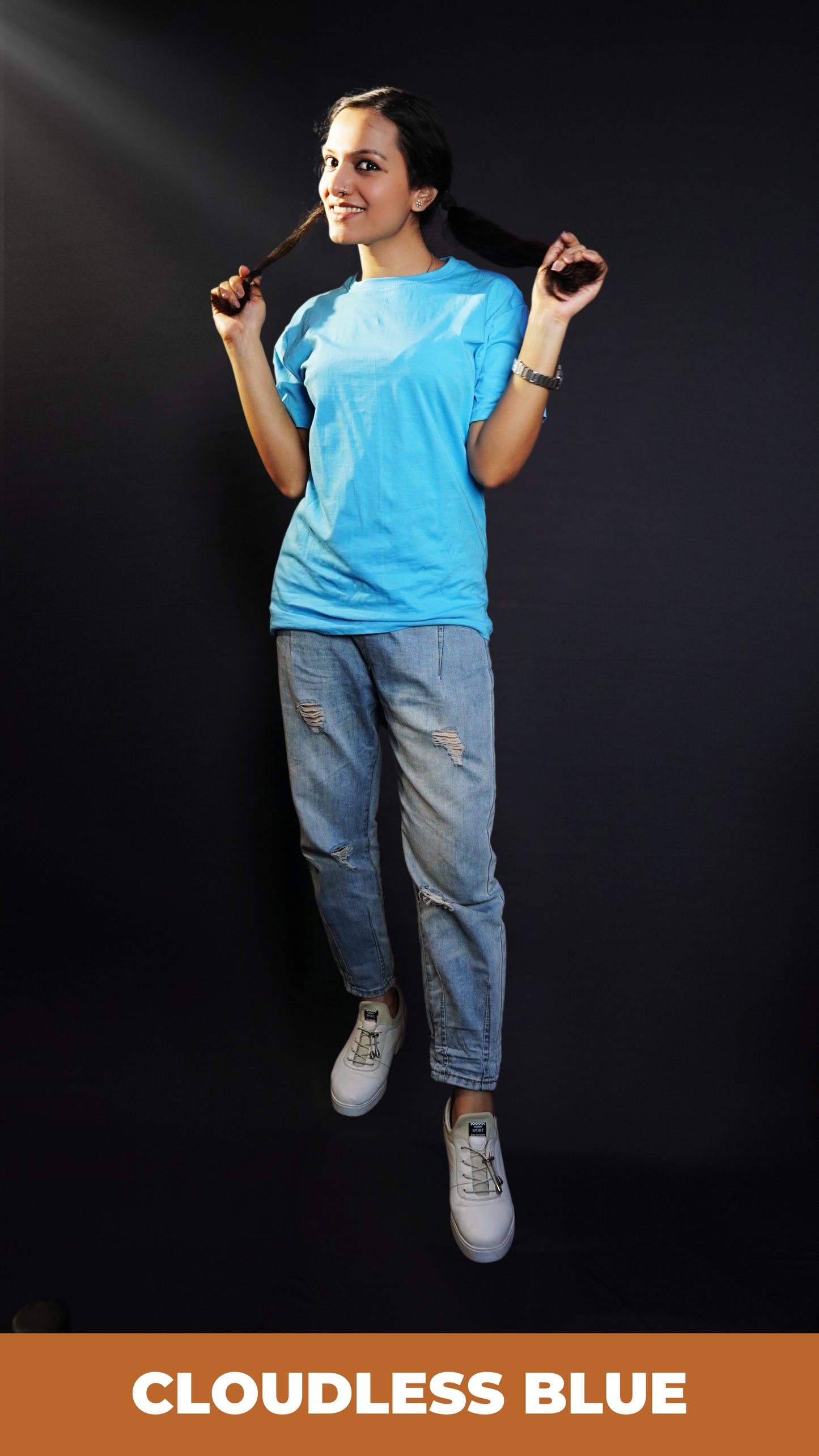 A woman posing with her hands grabbing last sections of her hair, smiling brightly, wearing a long round neck plain t-shirt in cloudless blue color, highlighting a funky easygoing fit-Muselot