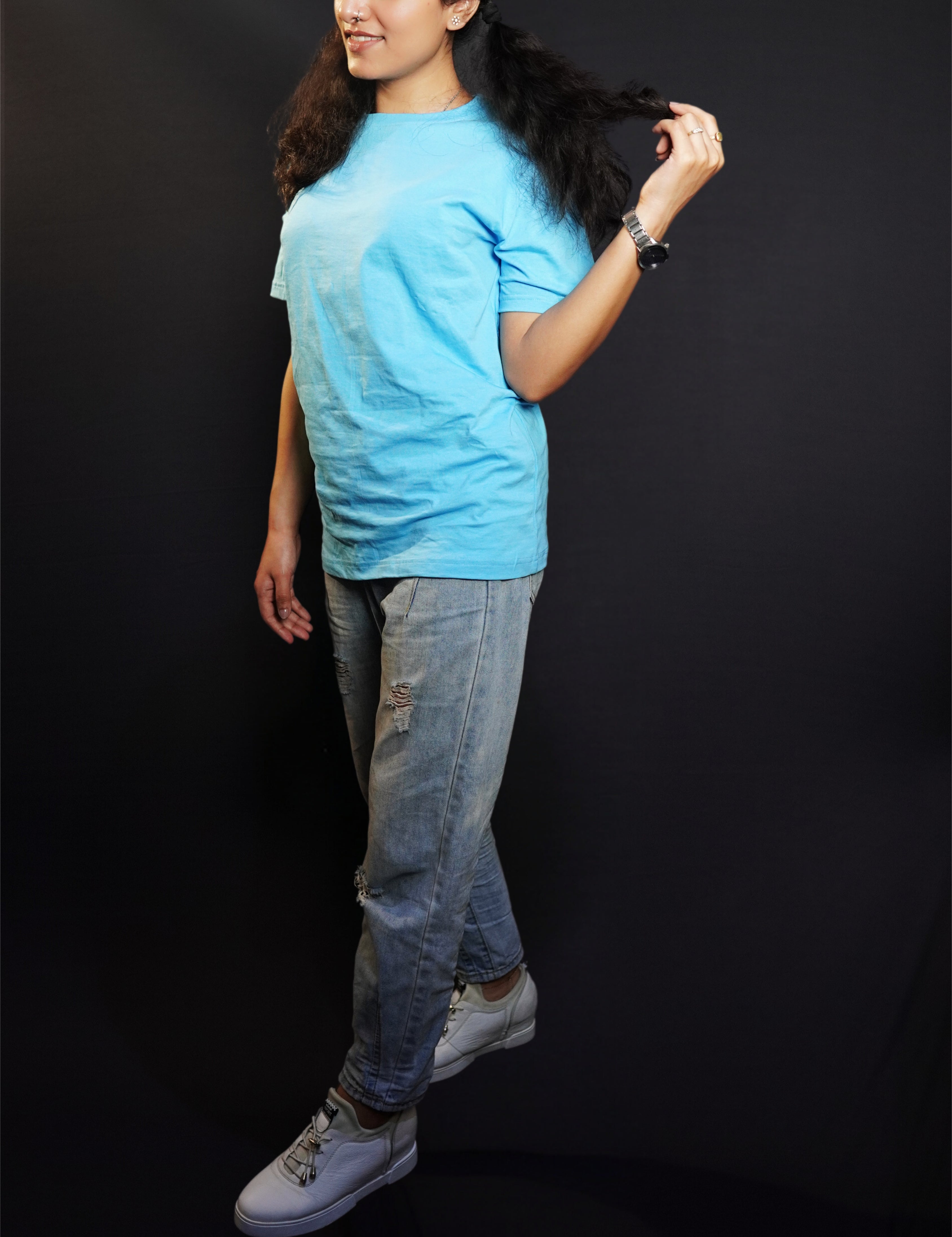 A stylish model standing sideways, pulling a tip of her hair, wearing a plain cloudless blue round neck t shirt showcasing a casual comfortable look-Muselot