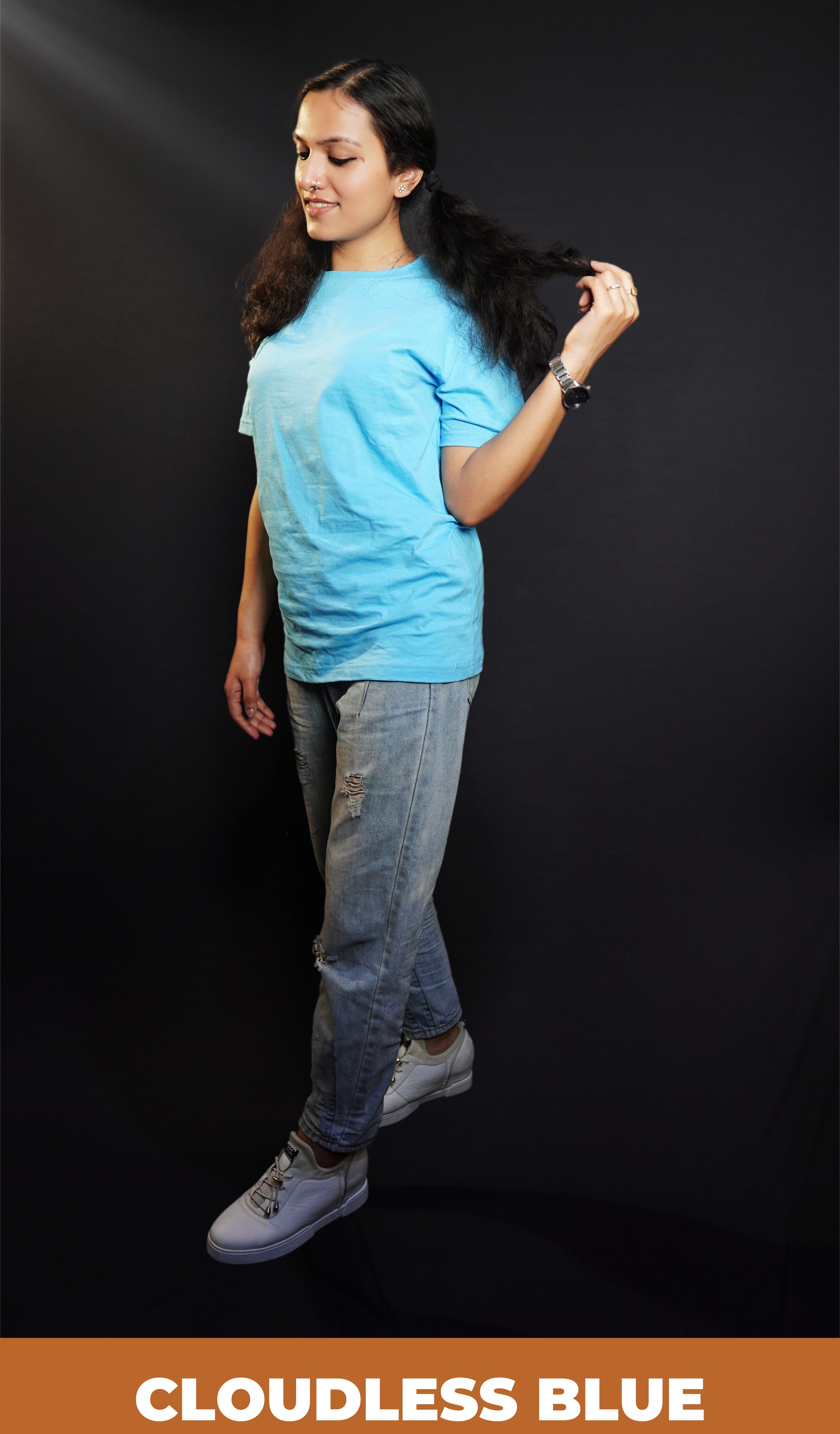 A stylish model standing sideways, pulling a tip of her hair, wearing a plain cloudless blue round neck t shirt showcasing a casual comfortable look-Muselot
