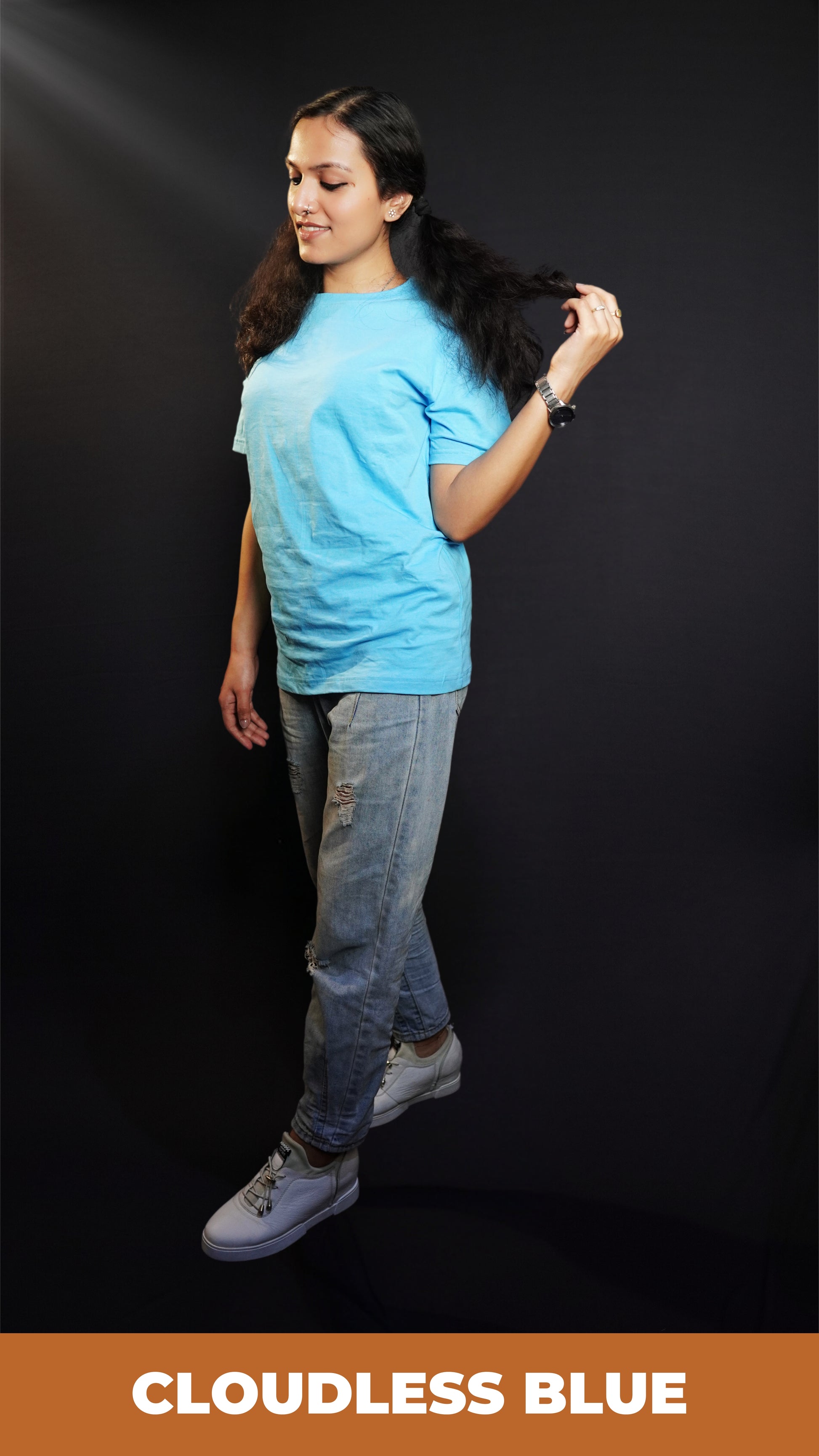 A stylish model standing sideways, pulling a tip of her hair, wearing a plain cloudless blue round neck t shirt showcasing a casual comfortable look-Muselot