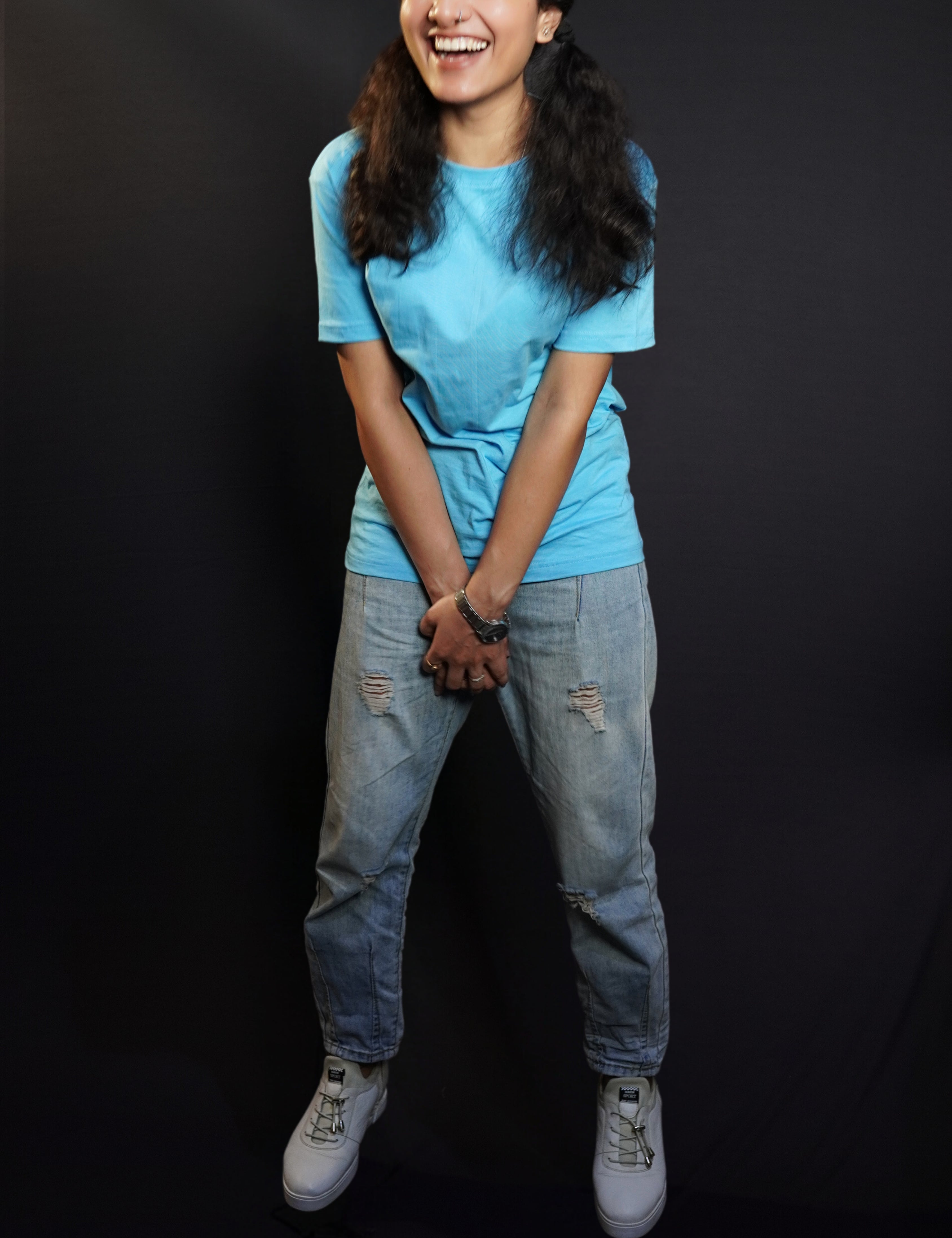 A woman wearing a plain long length cloudless blue t shirt holding her both hands as she laughs out loud, highlighting a casual easy fit-Muselot