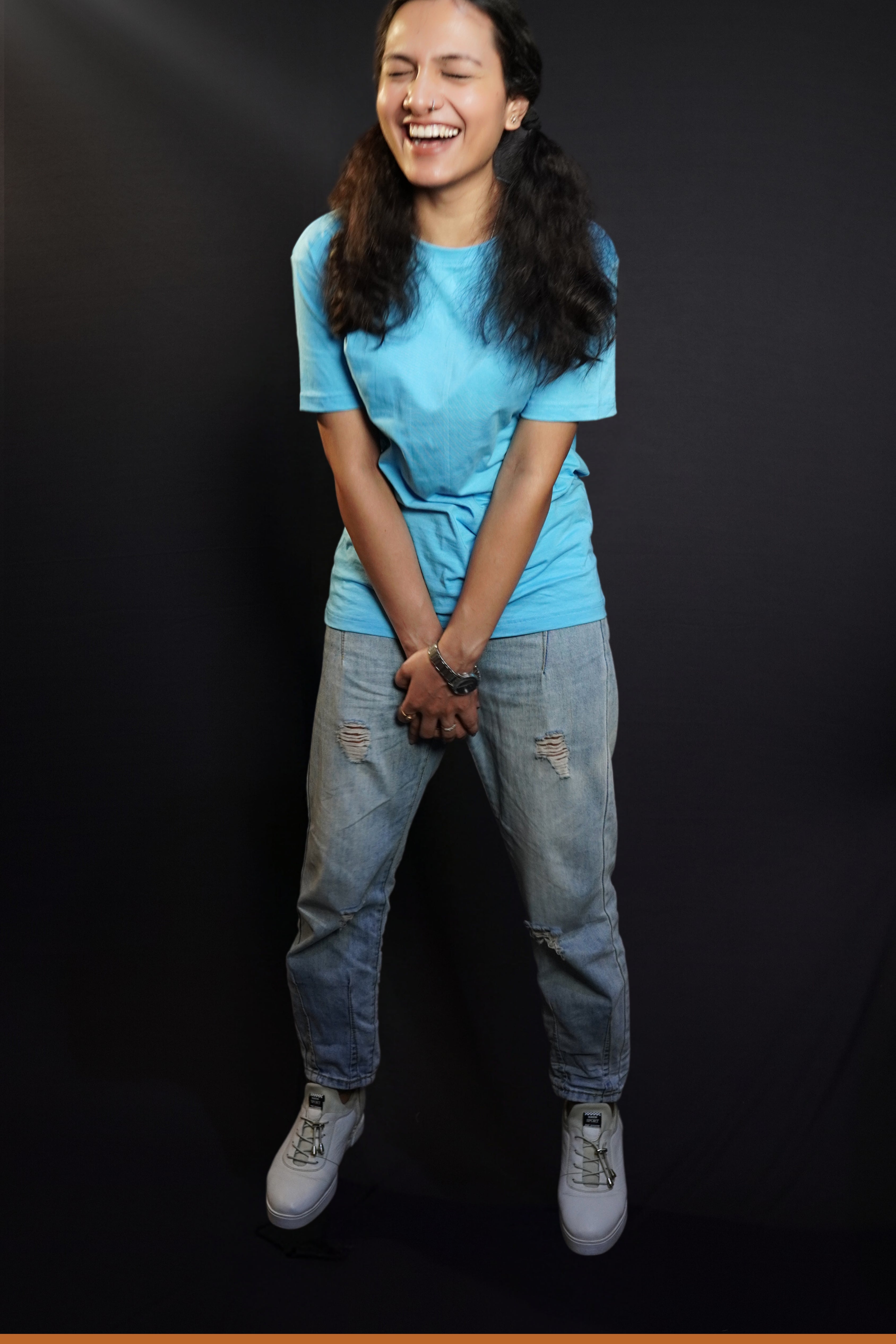 A woman wearing a plain long length cloudless blue t shirt holding her both hands as she laughs out loud, highlighting a casual easy fit-Muselot