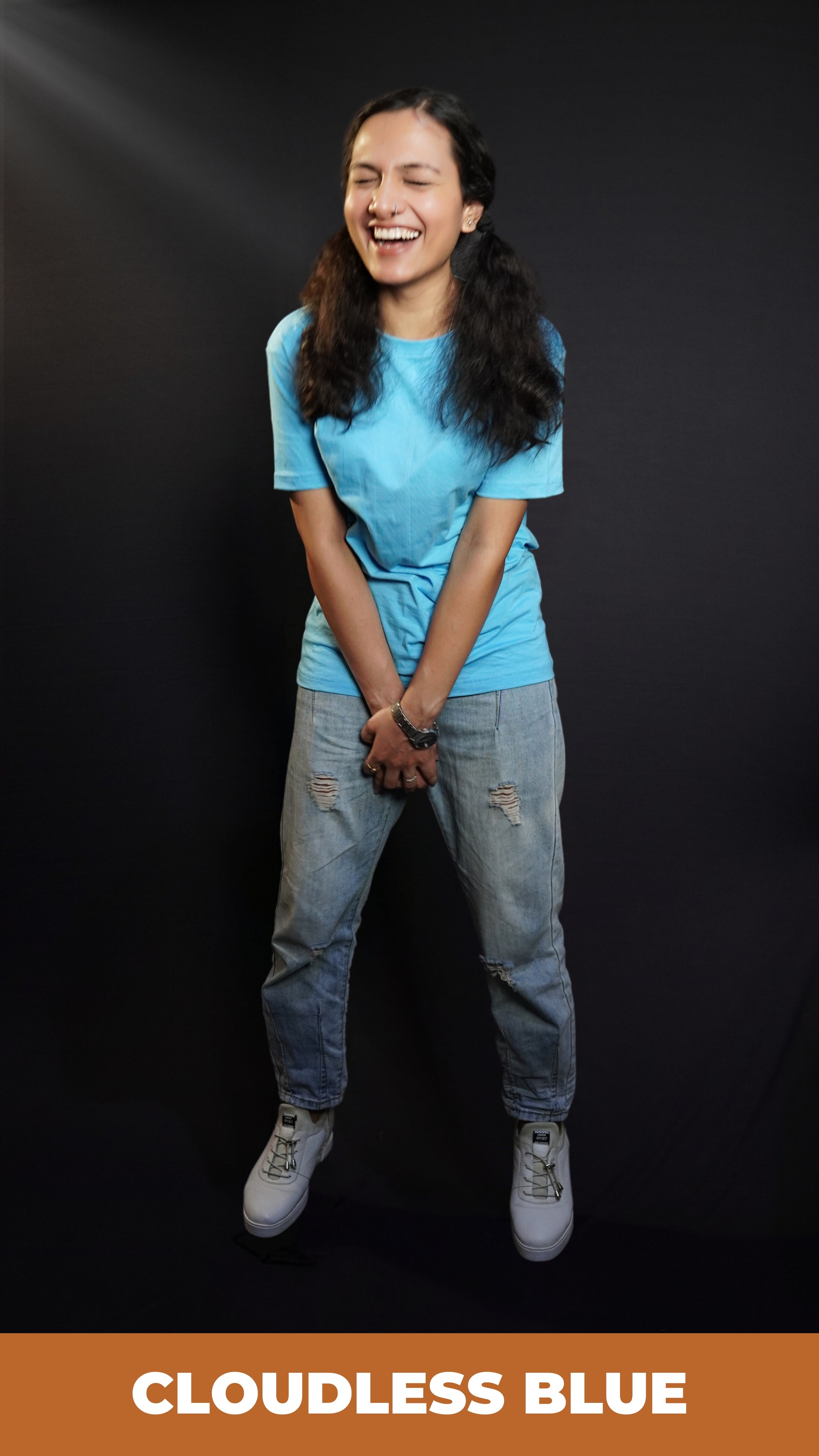 A woman wearing a plain long length cloudless blue t shirt holding her both hands as she laughs out loud, highlighting a casual easy fit-Muselot