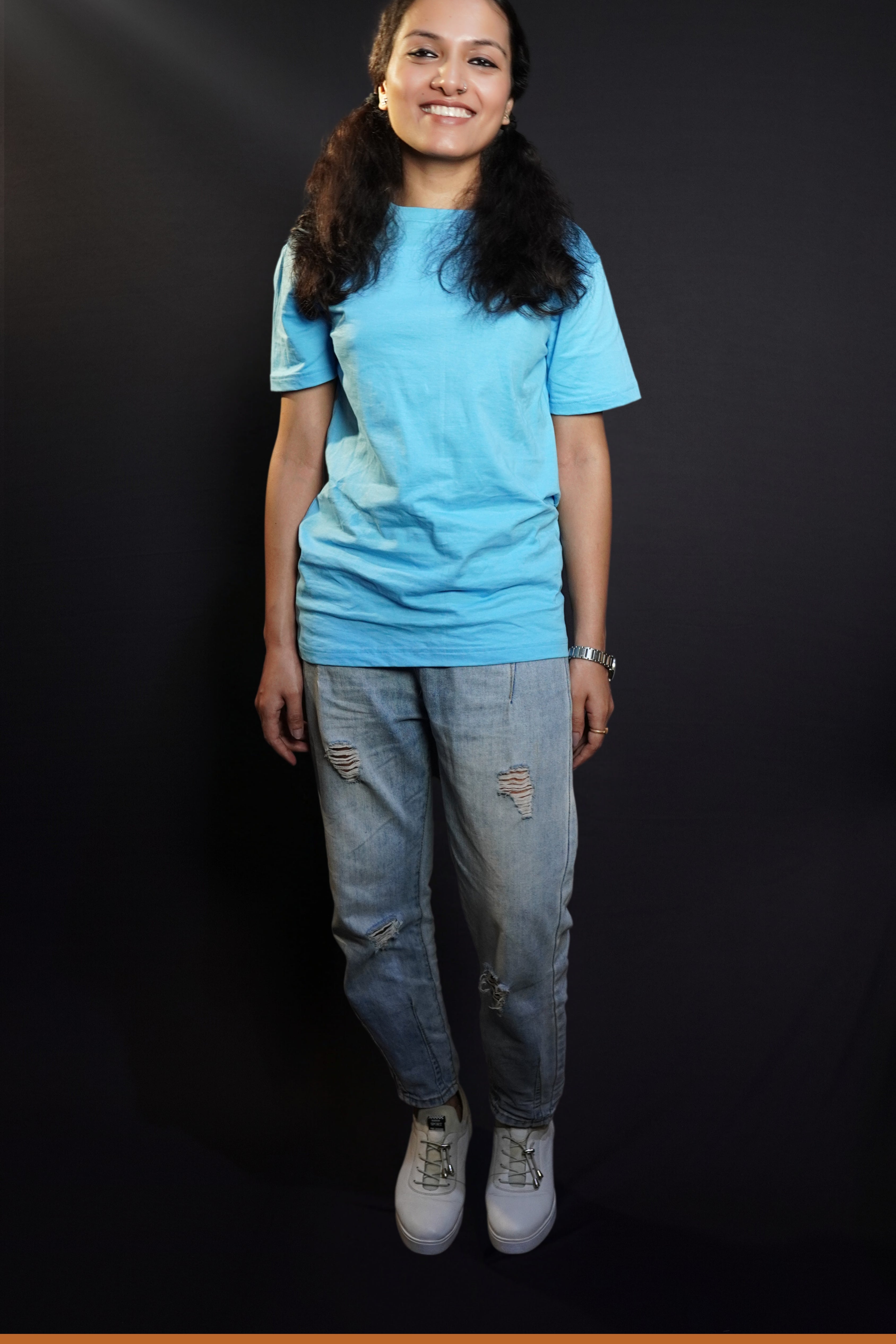 A woman smiling brightly in a plain cotton long length clouldless blue t-shirt, standing in a relaxed way, showcasing a casual popular style-Muselot