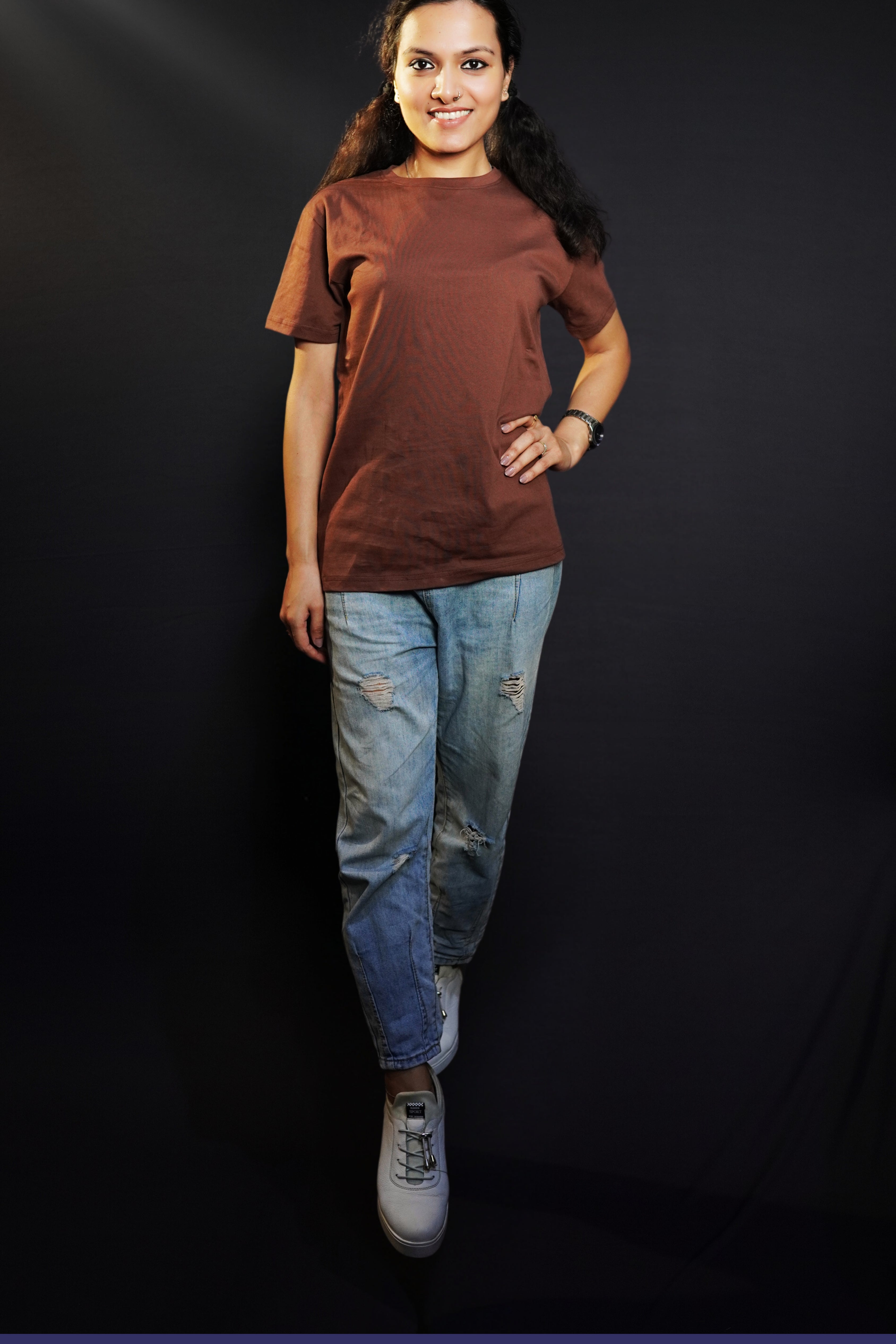 A woman posing happily with her one hand on her waist and other on her side, wearing a round neck plain long length t-shirt, highlighting a soft flexible style-Muselot