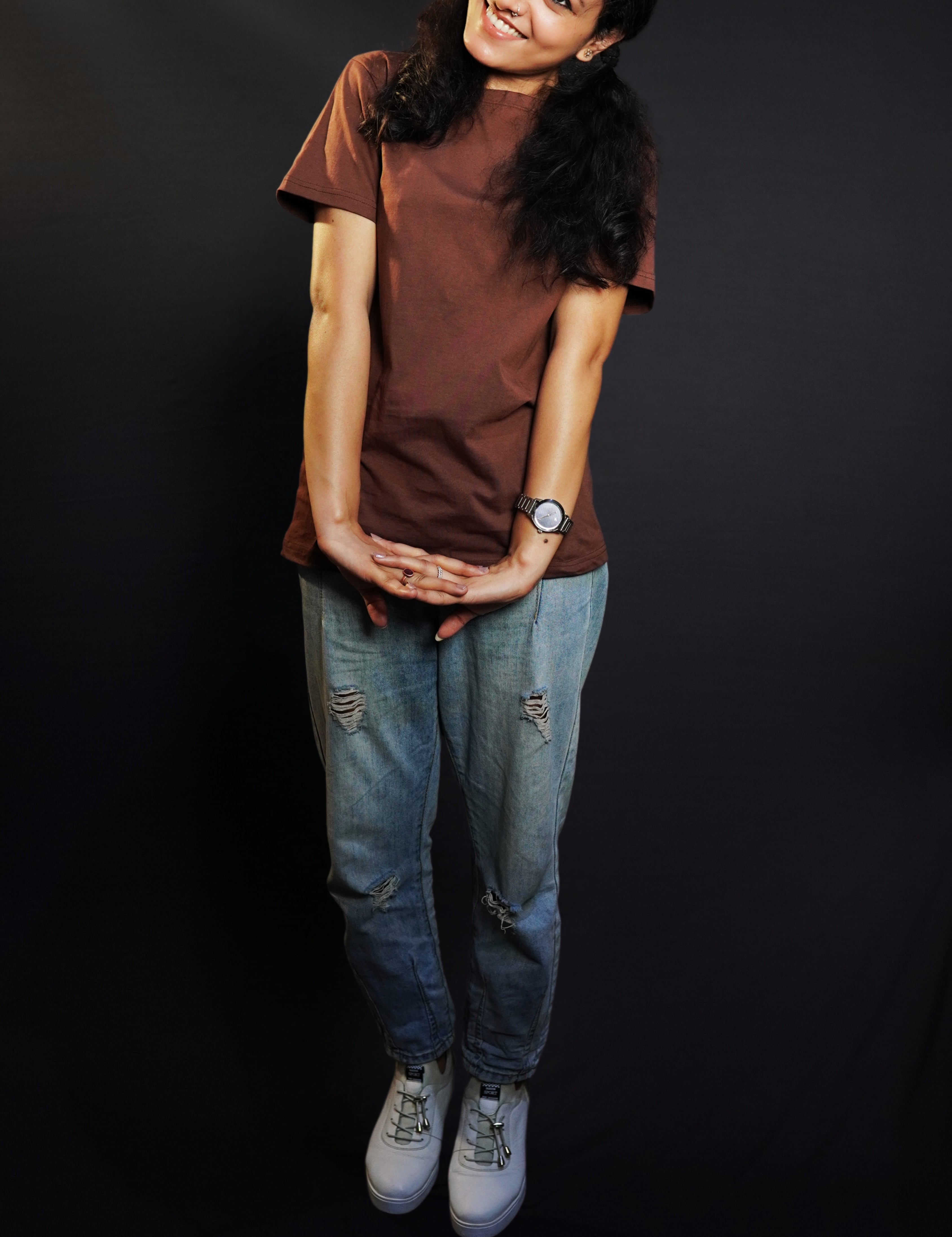 A woman wearing a short sleeved cotton coffee brown plain t-shirt, posing with her hands stretched and fingers intertwined, highlighting a fashionable casual fit-Muselot