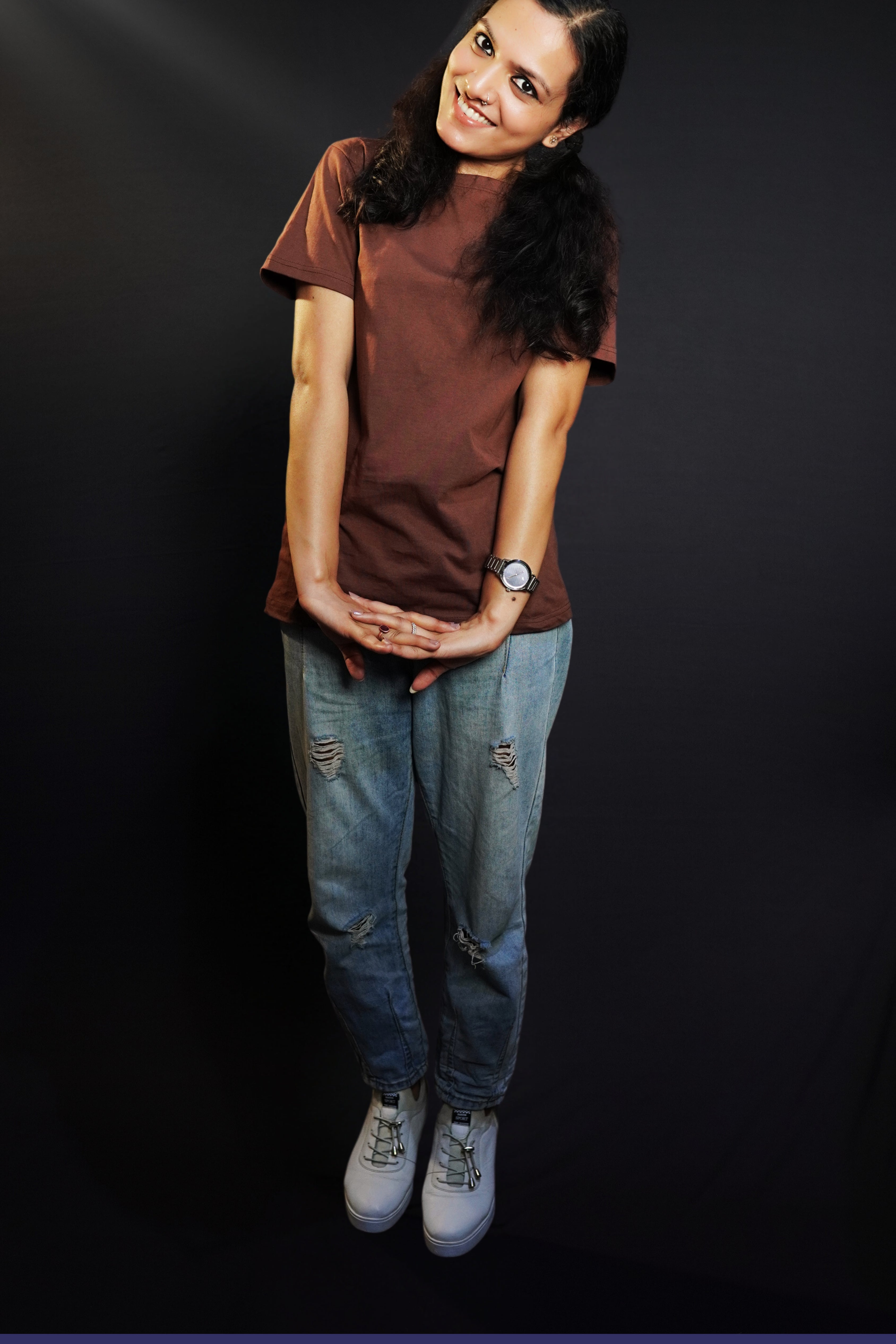 A woman wearing a short sleeved cotton coffee brown plain t-shirt, posing with her hands stretched and fingers intertwined, highlighting a fashionable casual fit-Muselot