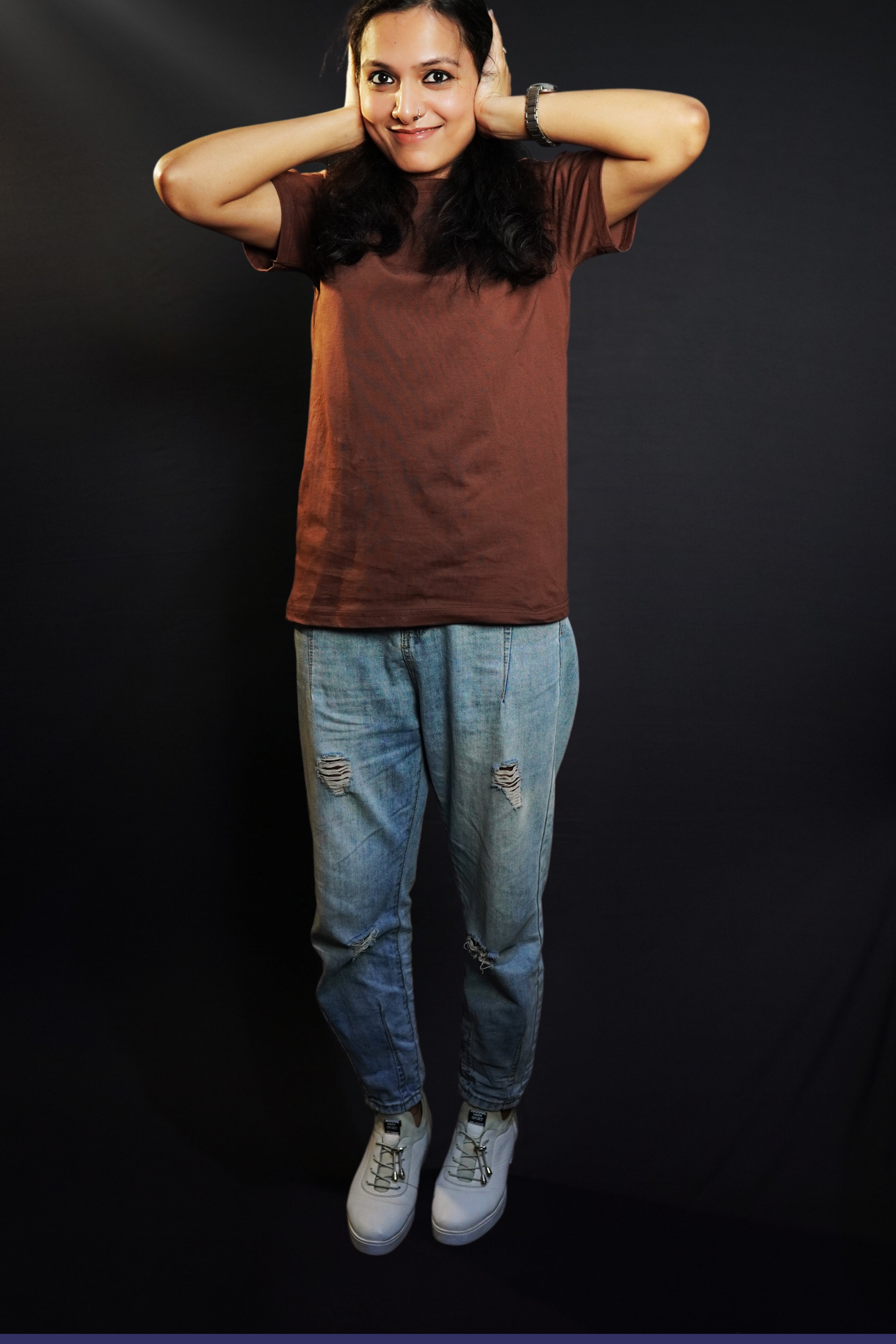 A woman wearing a coffee brown plain stretchable short sleeved t-shirt, posing with her hands on her ears, showcasing a roomy comfortable fit-Muselot