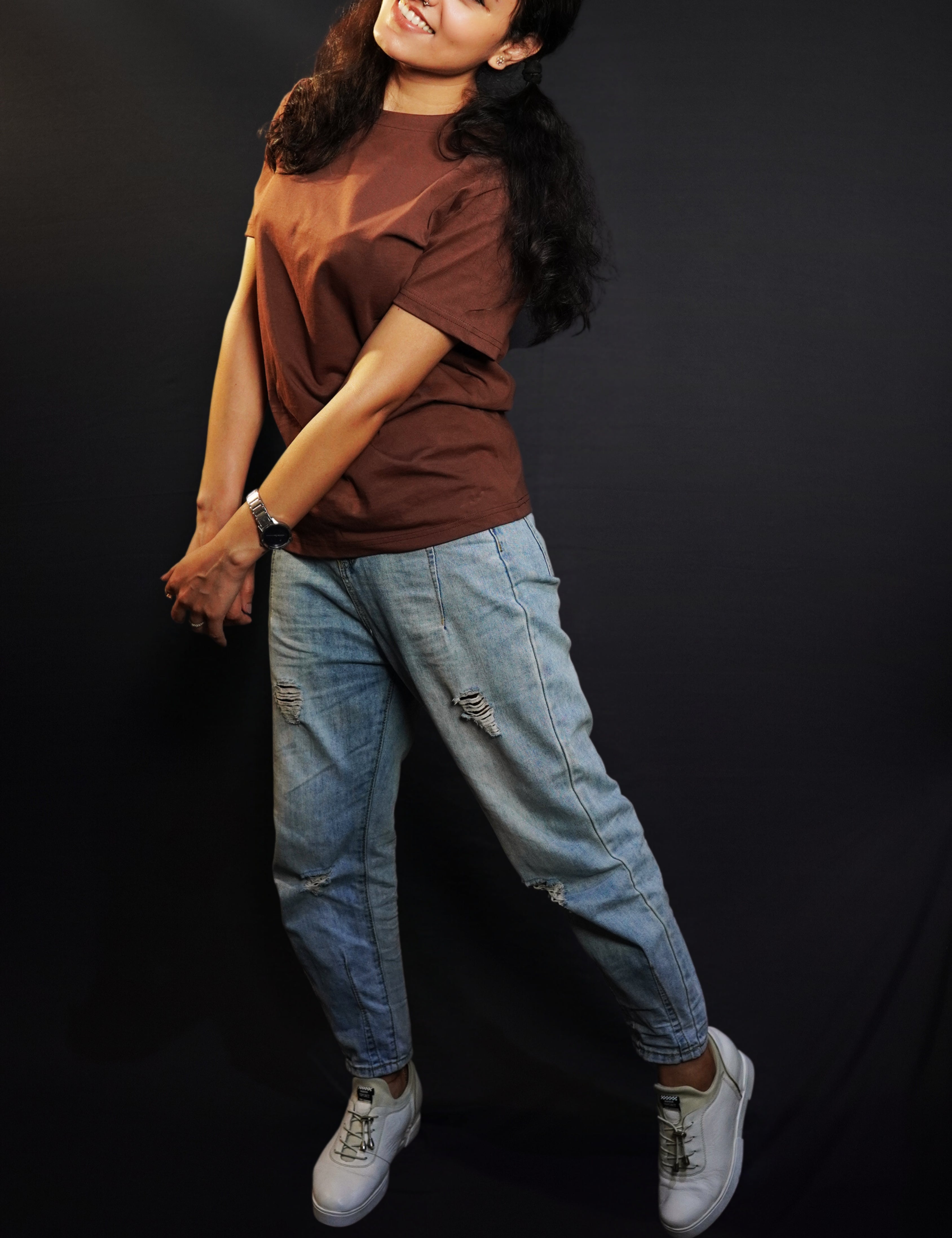 A woman posing happily as she sways sideways with her head bent backward, wearing a unisex stretchable round neck coffee brown t-shirt, showcasing a perfect fit style-Muselot
