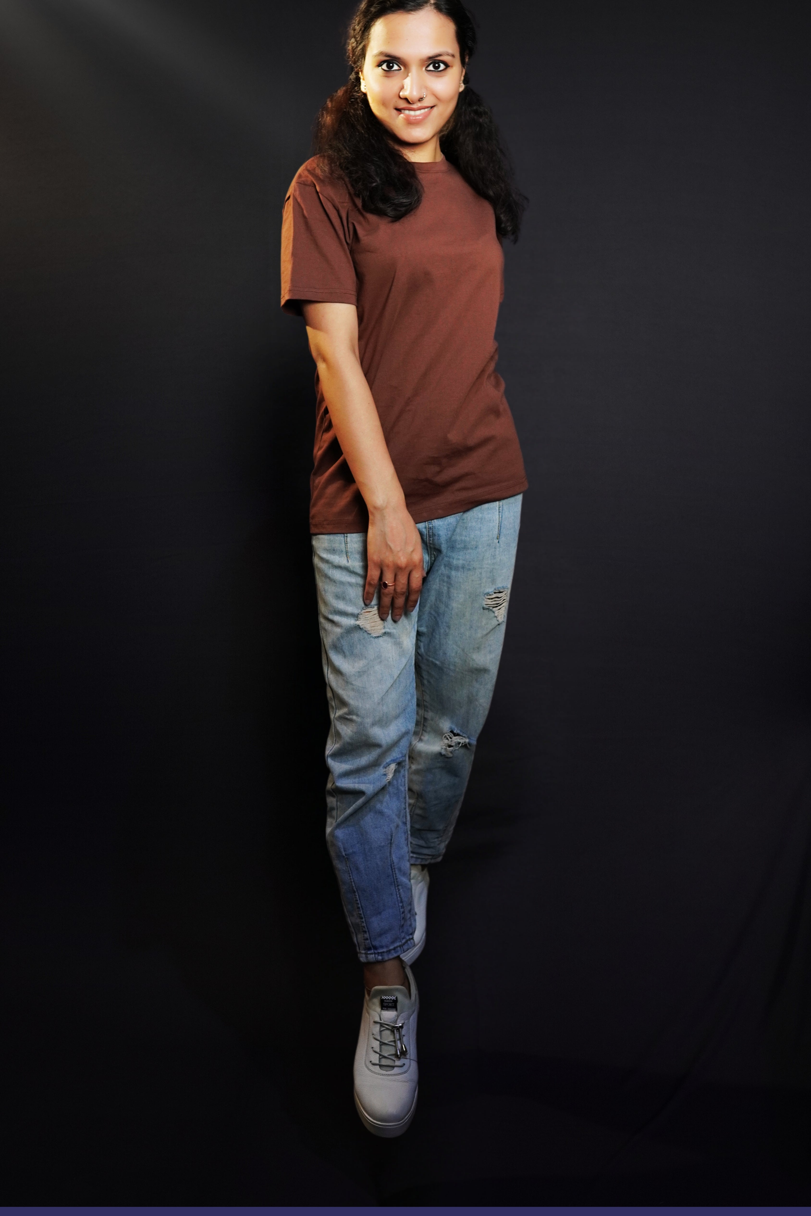 An elegant model posing with her one hand on top of her thigh and other behind her, wearing a cotton unisex plus size summer coffee brown t-shirt, showcasing a modish laid back fit-Muselot