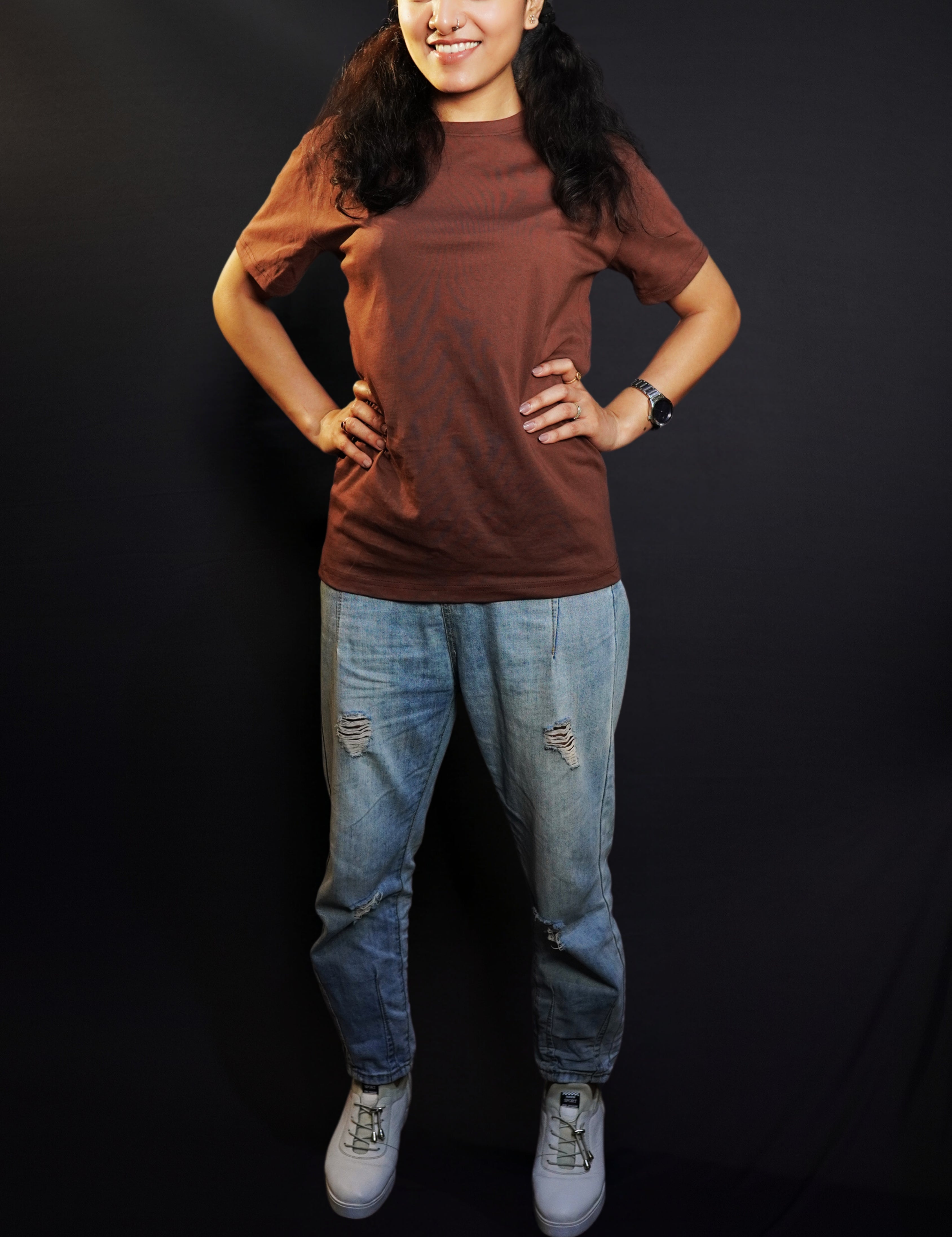 A woman wearing a long plain round neck coffee brown t-shirt, posing with her hands on the sides of her waist, showcasing a flowing voguish style-Muselot
