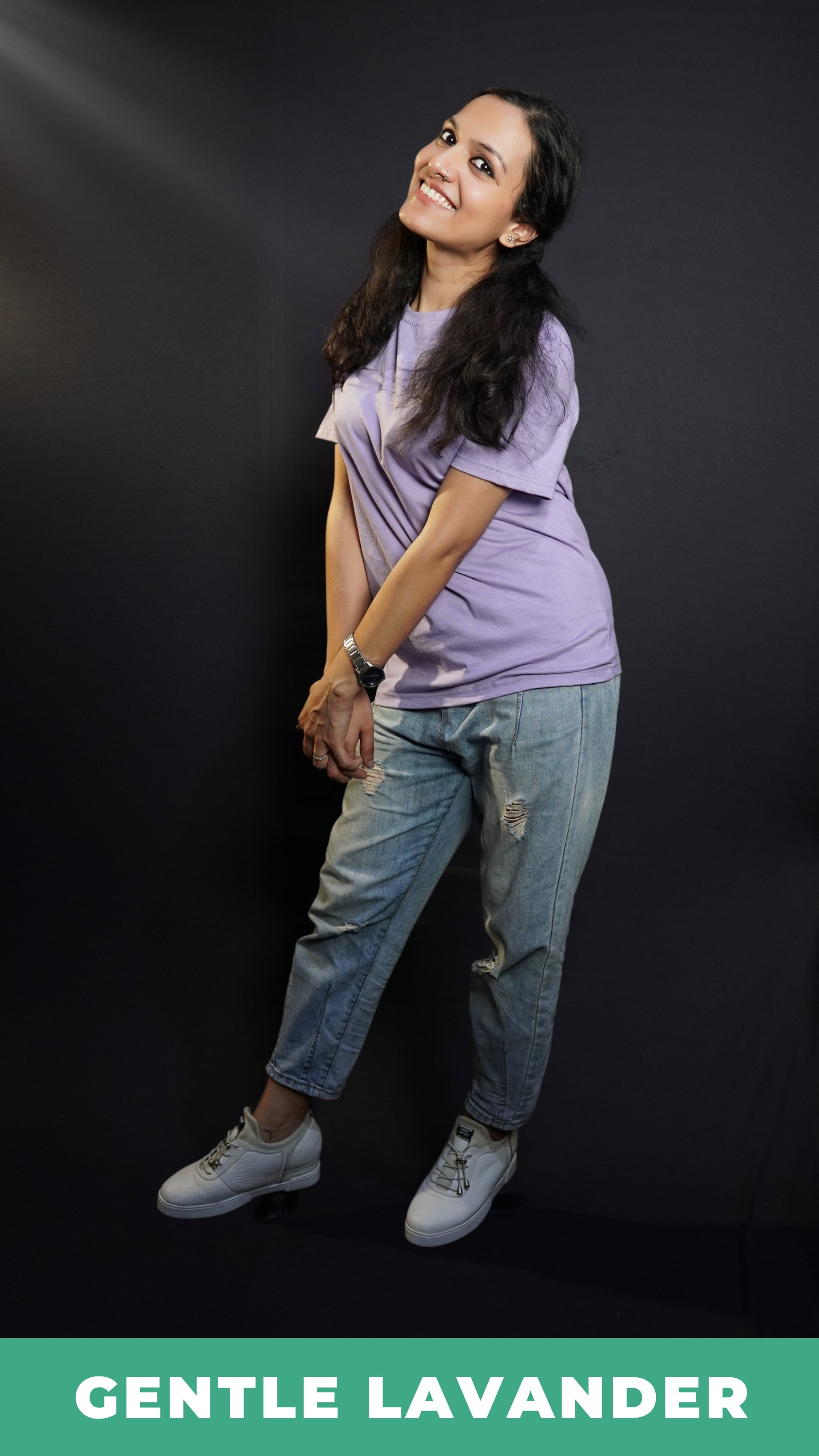 A woman standing sideways against a dark background in a men's cotton stretchable t-shirt, posing by grabbing her hands together, highlighting a popular casual fit-Muselot