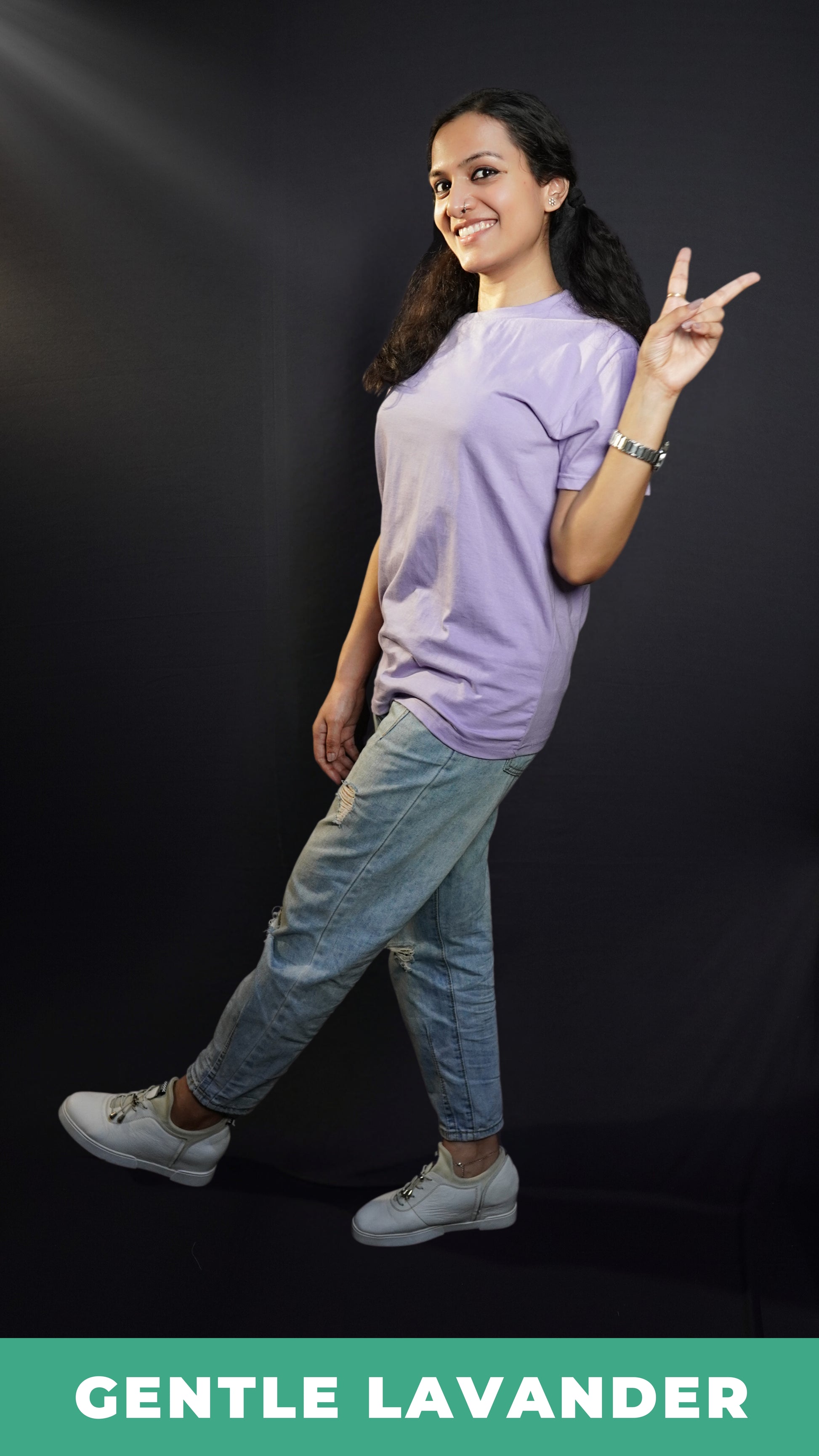 A woman wearing a gentle lavender long length round neck plain t-shirt, posing with her one hand making a v sign, standing sideways, showcasing a cool easygoing fit-Muselot