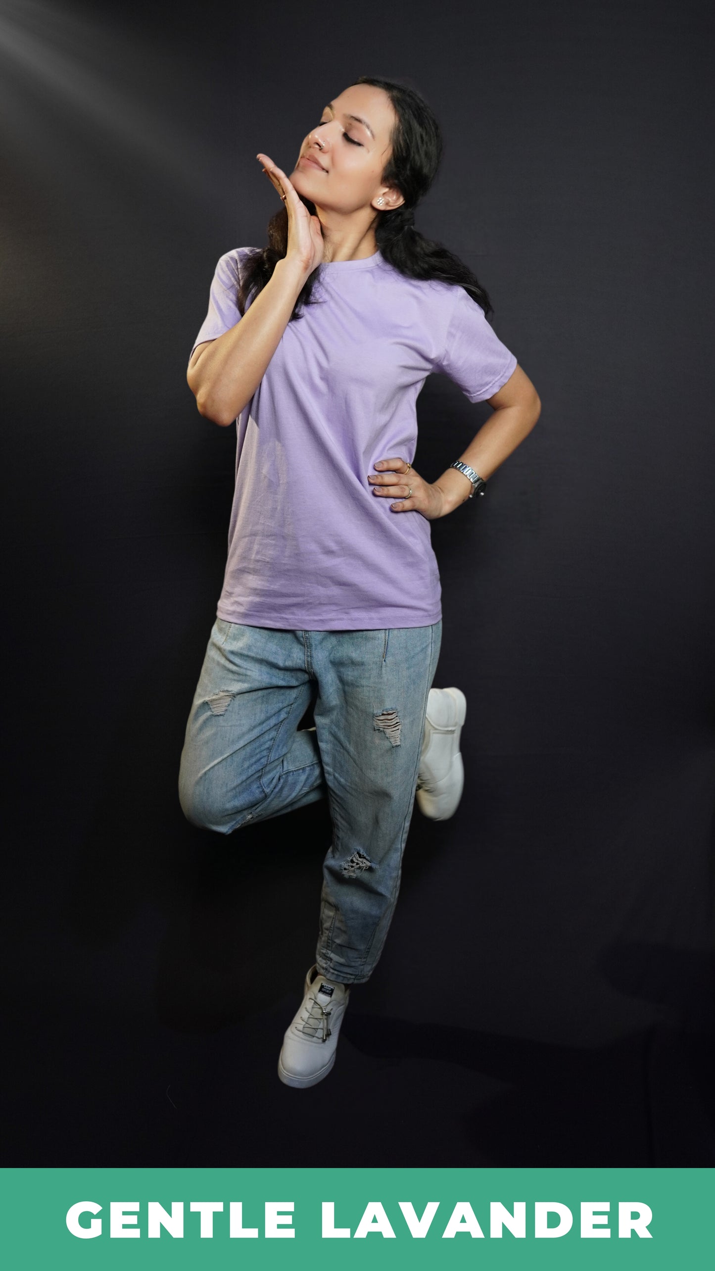 A stylish model posing with her hand sideway and below her chin, wearing a long length cotton plain round neck gentle lavender t-shirt, showcasing a flowing modish style-Muselot