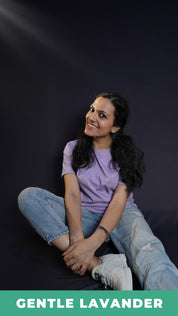 A stylish model wearing a plain short sleeved round neck t-shirt, posing by sitting against a dark background grabbing her leg gently with both hands, showcasing a swank perfect fit-Muselot