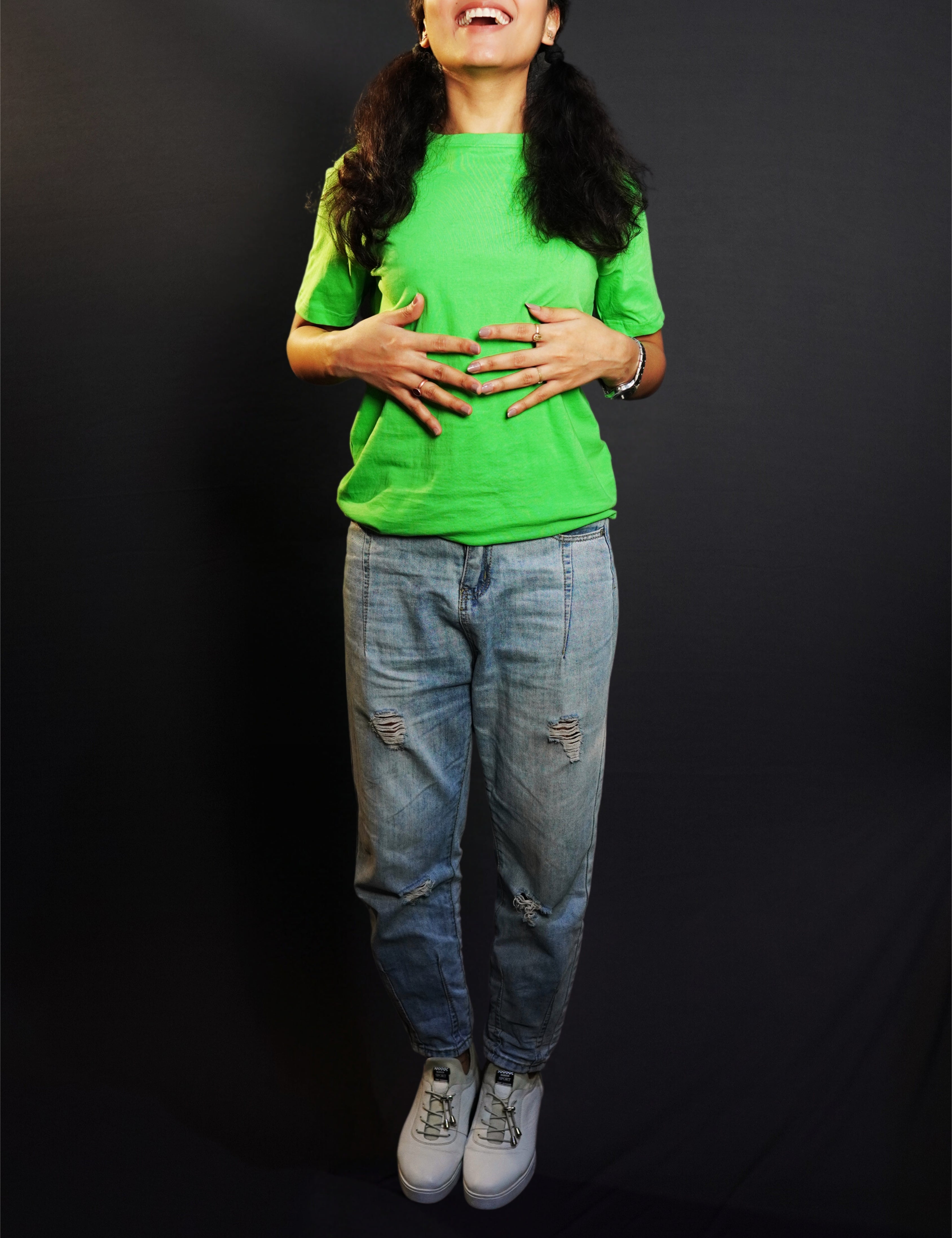 A woman laughing happily standing against a dark background as her hands gently lie on her stomach, wearing a liril green plain unisex round neck short sleeves t-shirt, showcasing a casual everyday look-Muselot