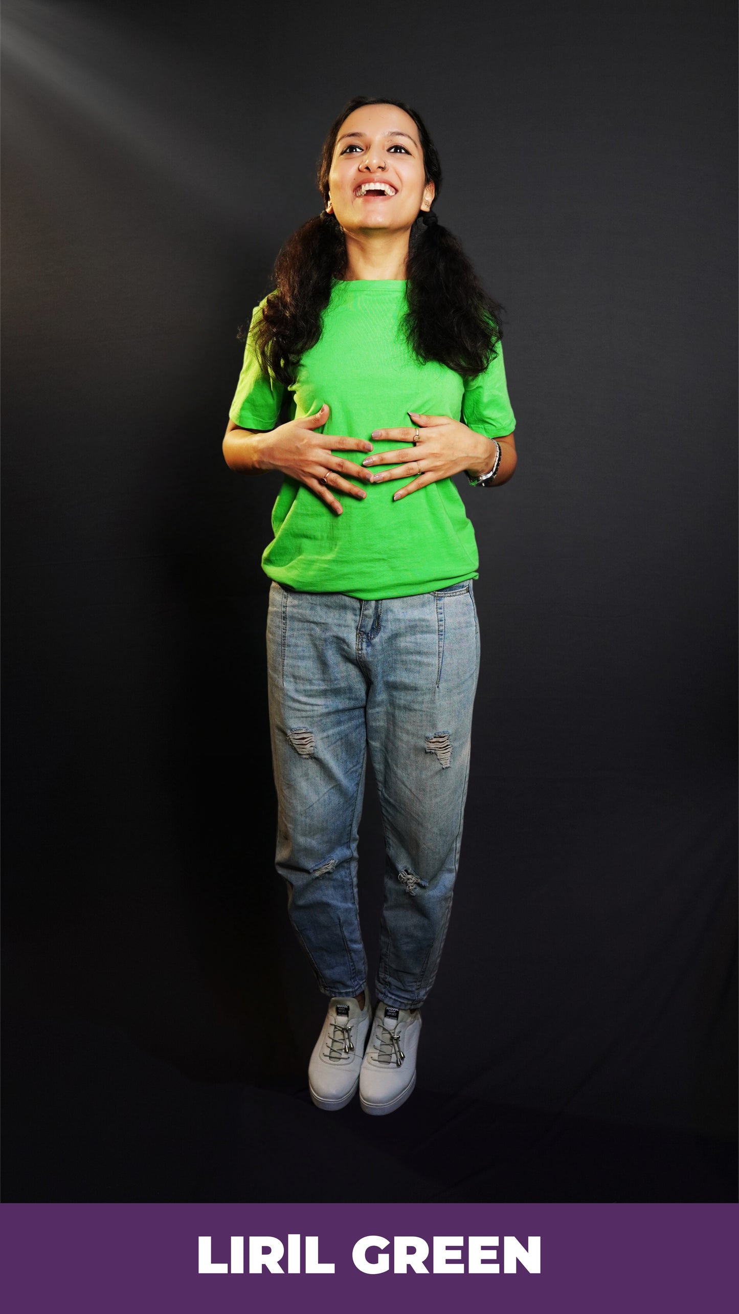 A woman laughing happily standing against a dark background as her hands gently lie on her stomach, wearing a liril green plain unisex round neck short sleeves t-shirt, showcasing a casual everyday look-Muselot