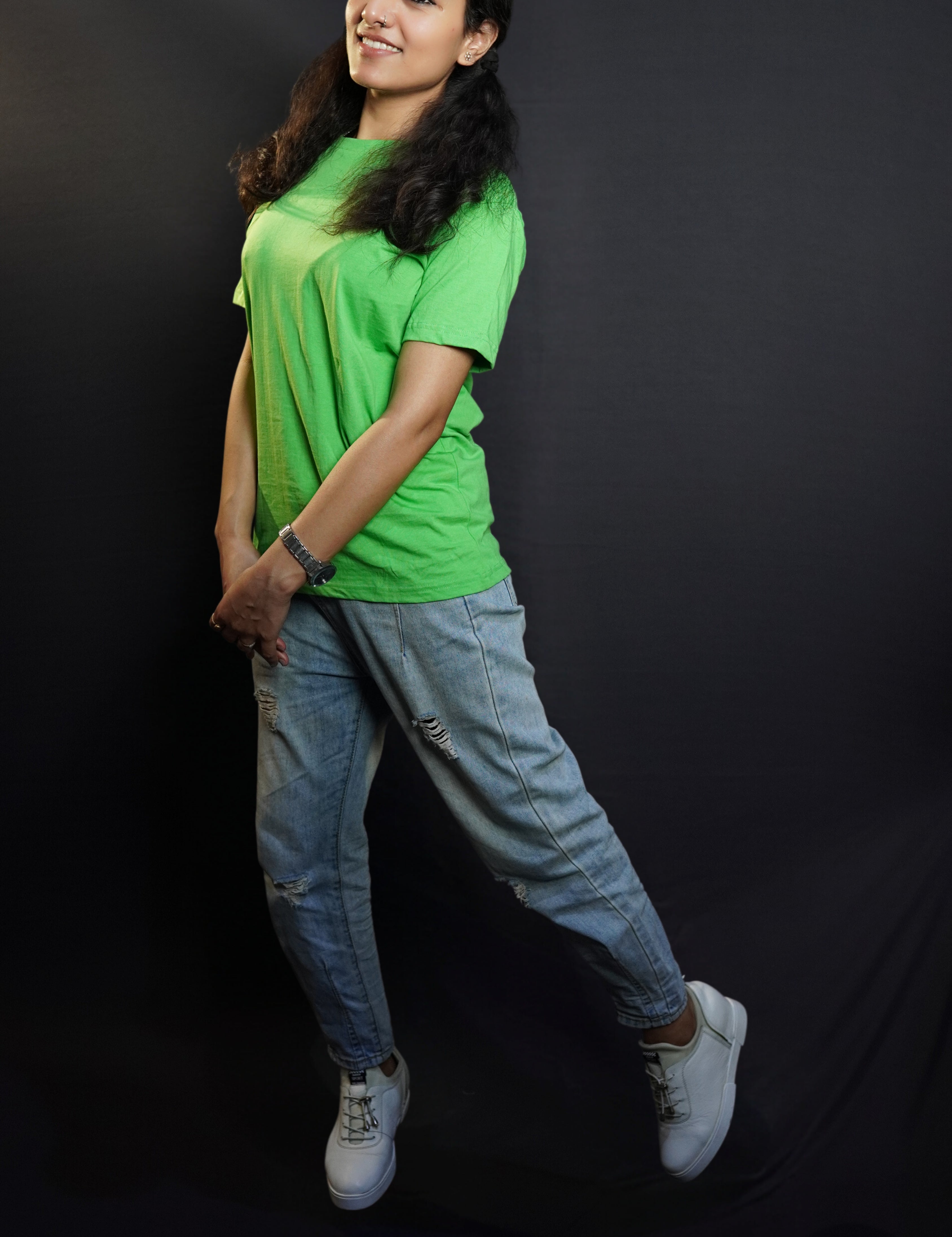 A smiling woman wearing a plus size lime green plain t-shirt with short sleeves and round neck, standing sideways as she sways slightly with her hands grabbing each other, showcasing a fashionable baggy fit-Muselot
