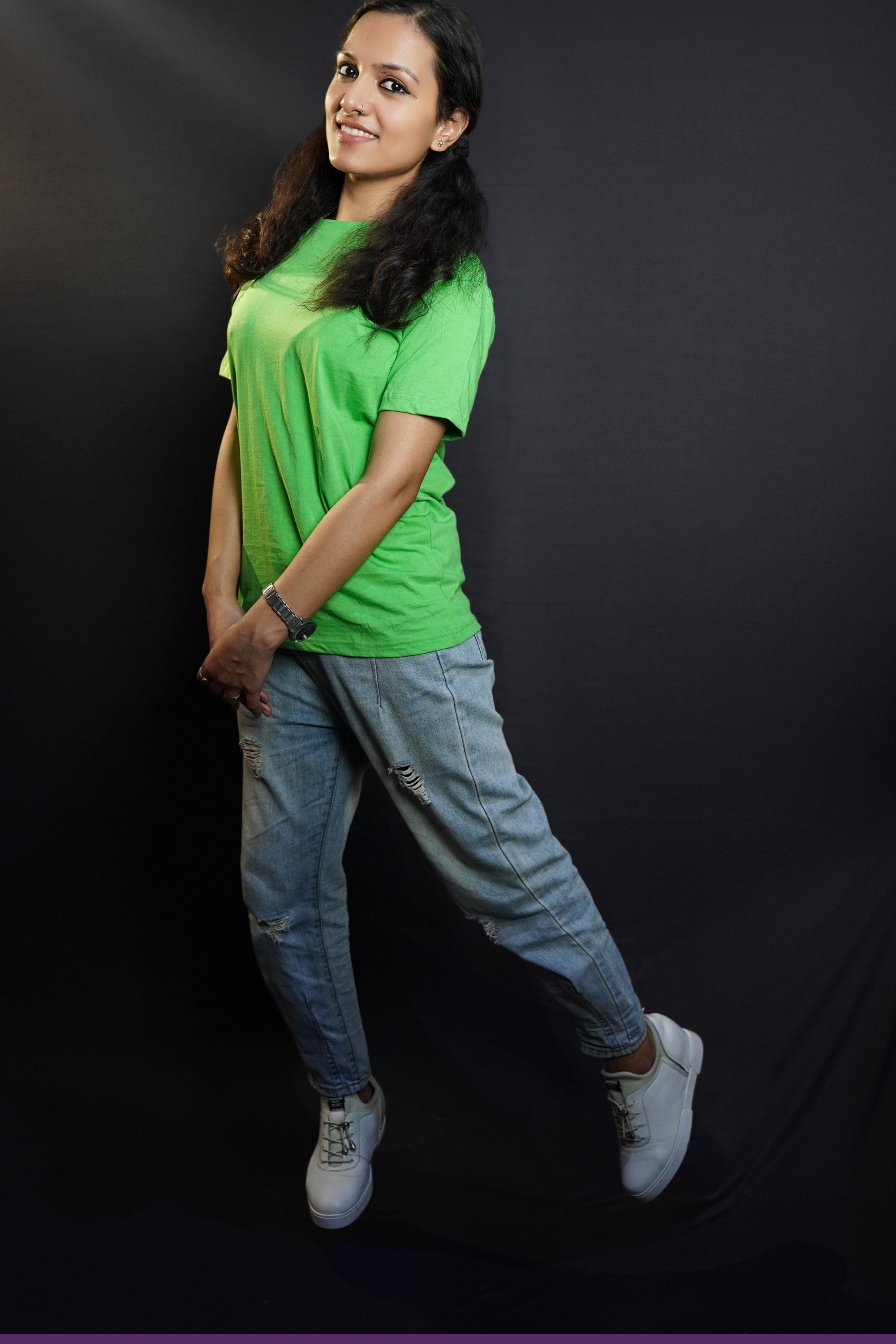 A smiling woman wearing a plus size lime green plain t-shirt with short sleeves and round neck, standing sideways as she sways slightly with her hands grabbing each other, showcasing a fashionable baggy fit-Muselot