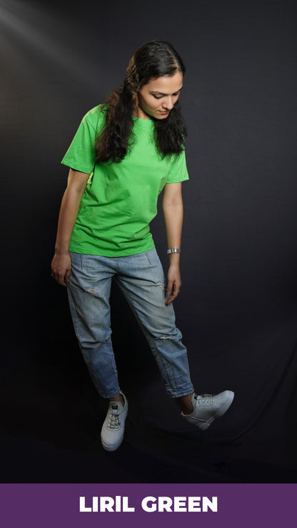 A woman wearing a women's long length short sleeved stretchable liril green t-shirt, posing against a dark background as she bends down slightly, looking at her white shoes, showcasing a relaxed cool fit-Muselot