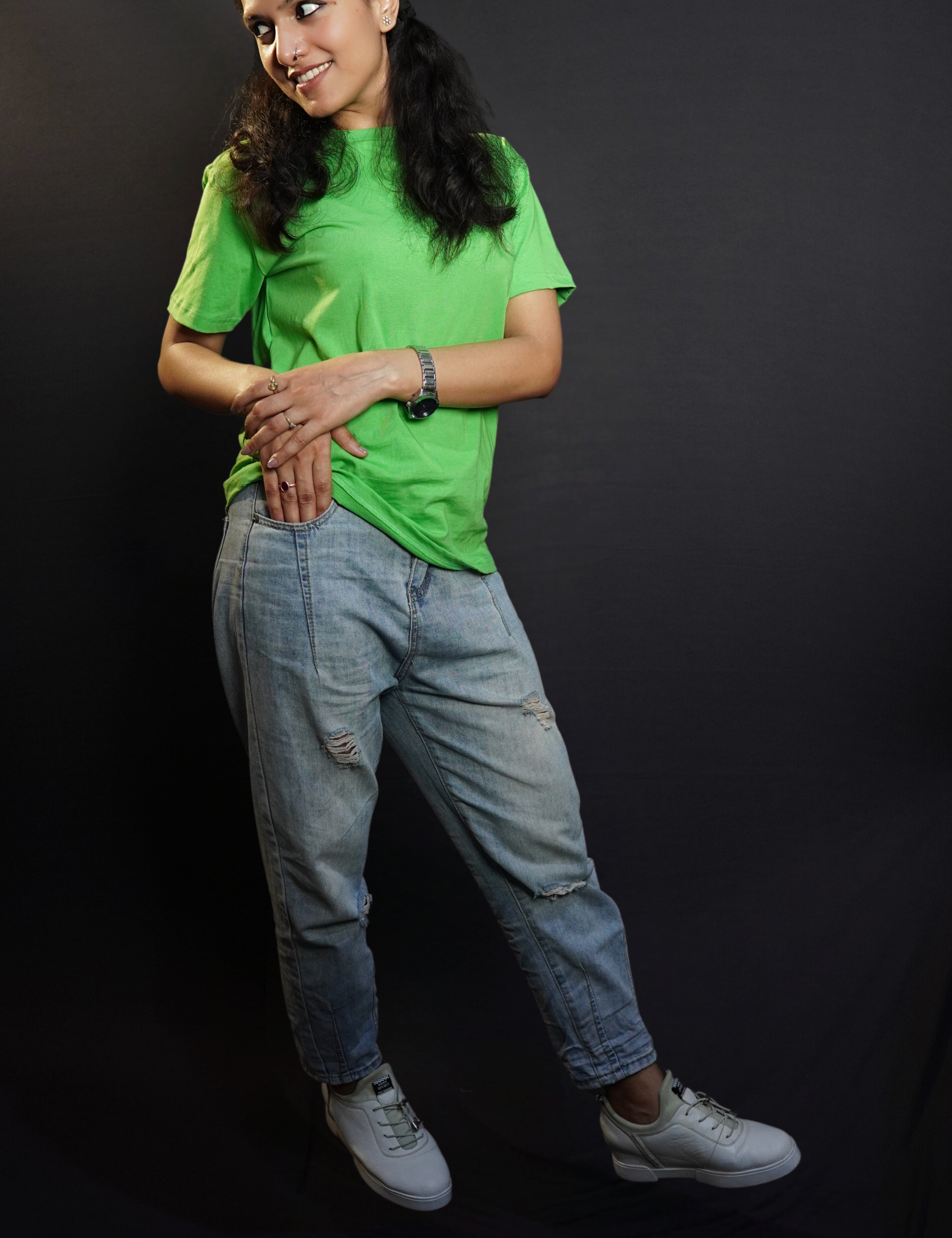 A stylish model posing happily with her hand about to go into the pocket of her jeans and another lying gently upon it, looking sideways, wearing a plain summer round neck moisture wicking lime green t-shirt, highlighting a voguish cozy look-Muselot