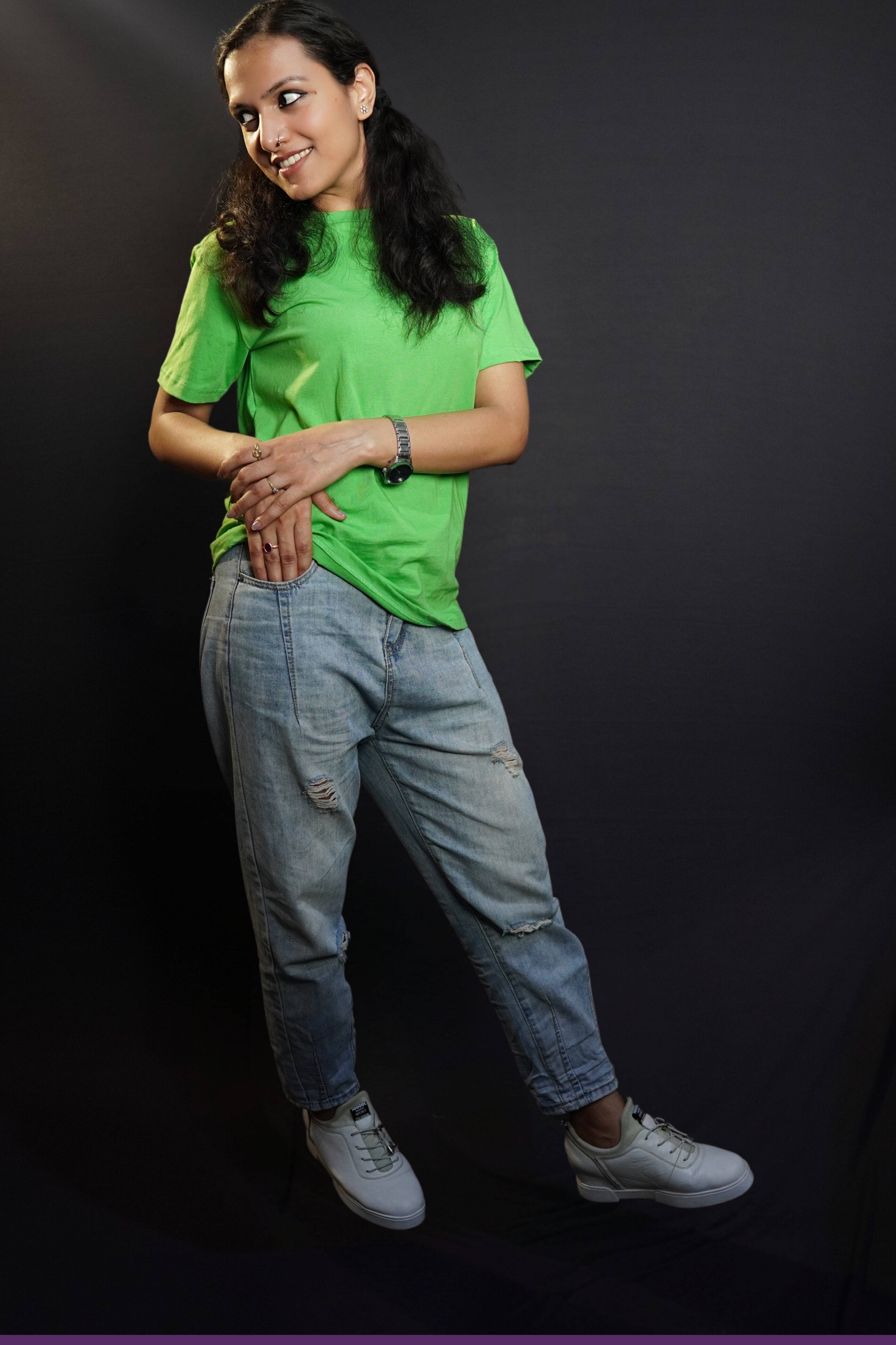 A stylish model posing happily with her hand about to go into the pocket of her jeans and another lying gently upon it, looking sideways, wearing a plain summer round neck moisture wicking lime green t-shirt, highlighting a voguish cozy look-Muselot
