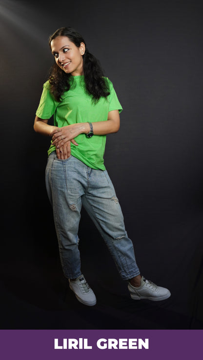 A stylish model posing happily with her hand about to go into the pocket of her jeans and another lying gently upon it, looking sideways, wearing a plain summer round neck moisture wicking lime green t-shirt, highlighting a voguish cozy look-Muselot