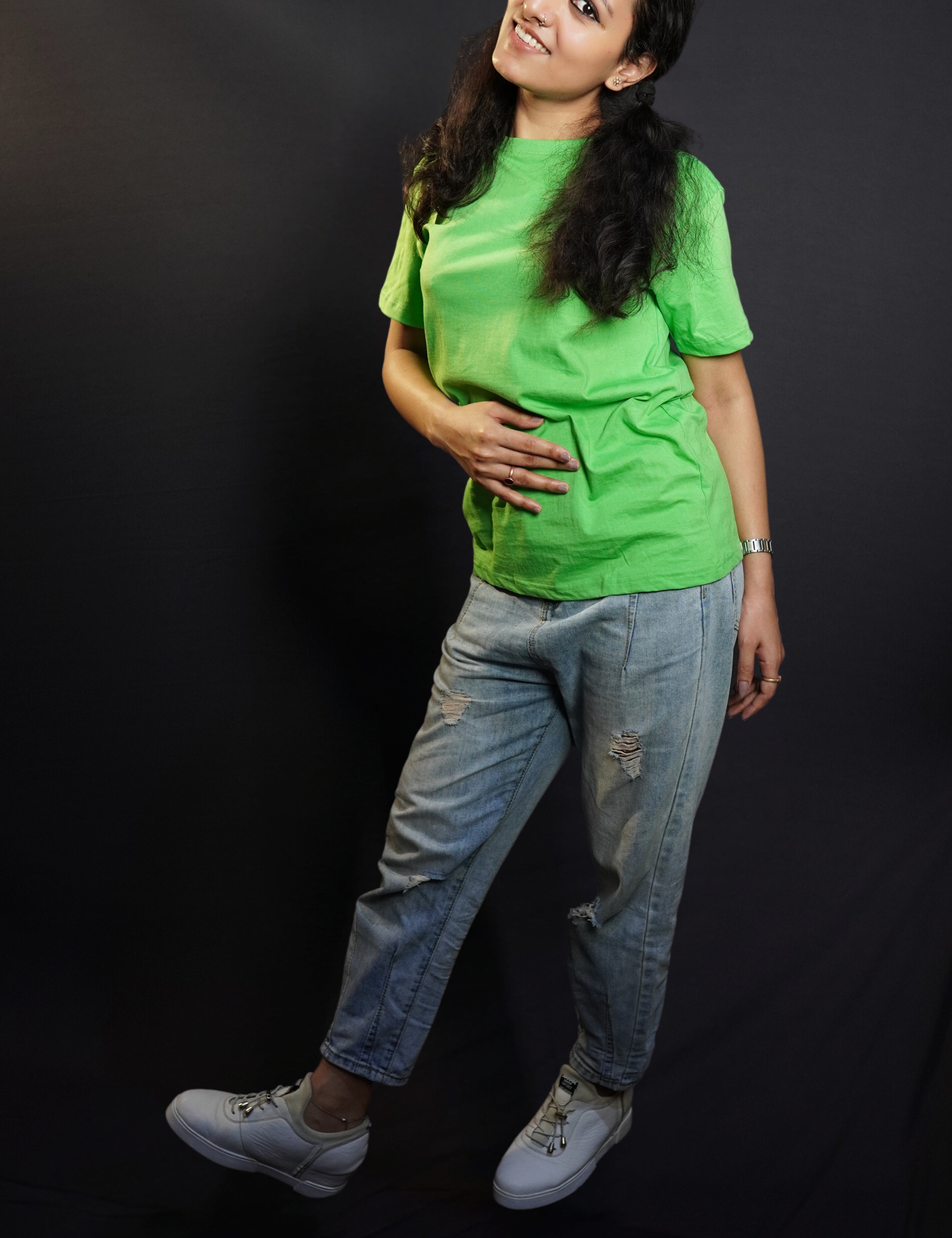 A woman in a long length unisex plain cotton liril green t-shirt, posing with her hand on her stomach and another behind her as she stands sideways, highlighting a modern comfortable fit-Muselot