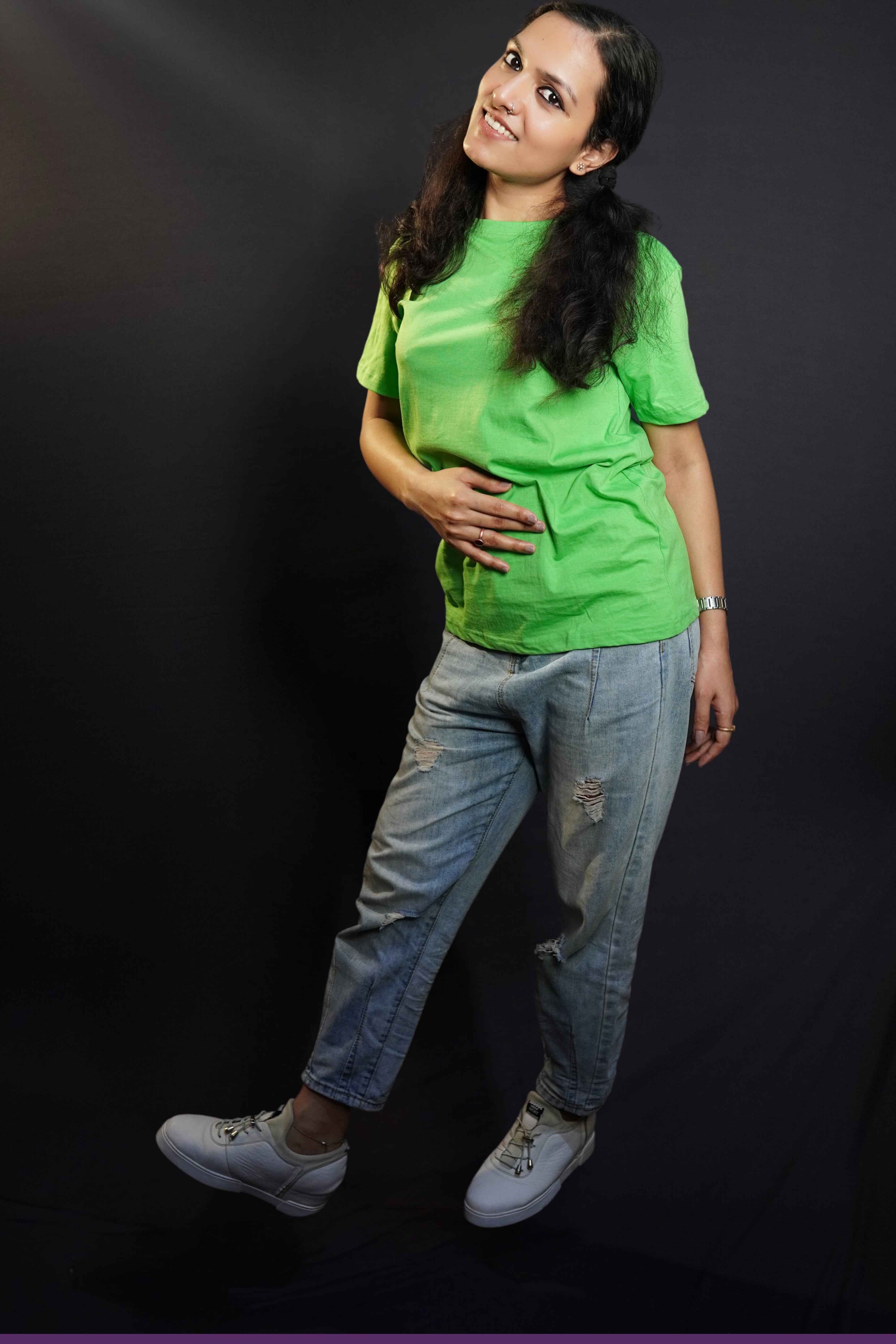 A woman in a long length unisex plain cotton liril green t-shirt, posing with her hand on her stomach and another behind her as she stands sideways, highlighting a modern comfortable fit-Muselot