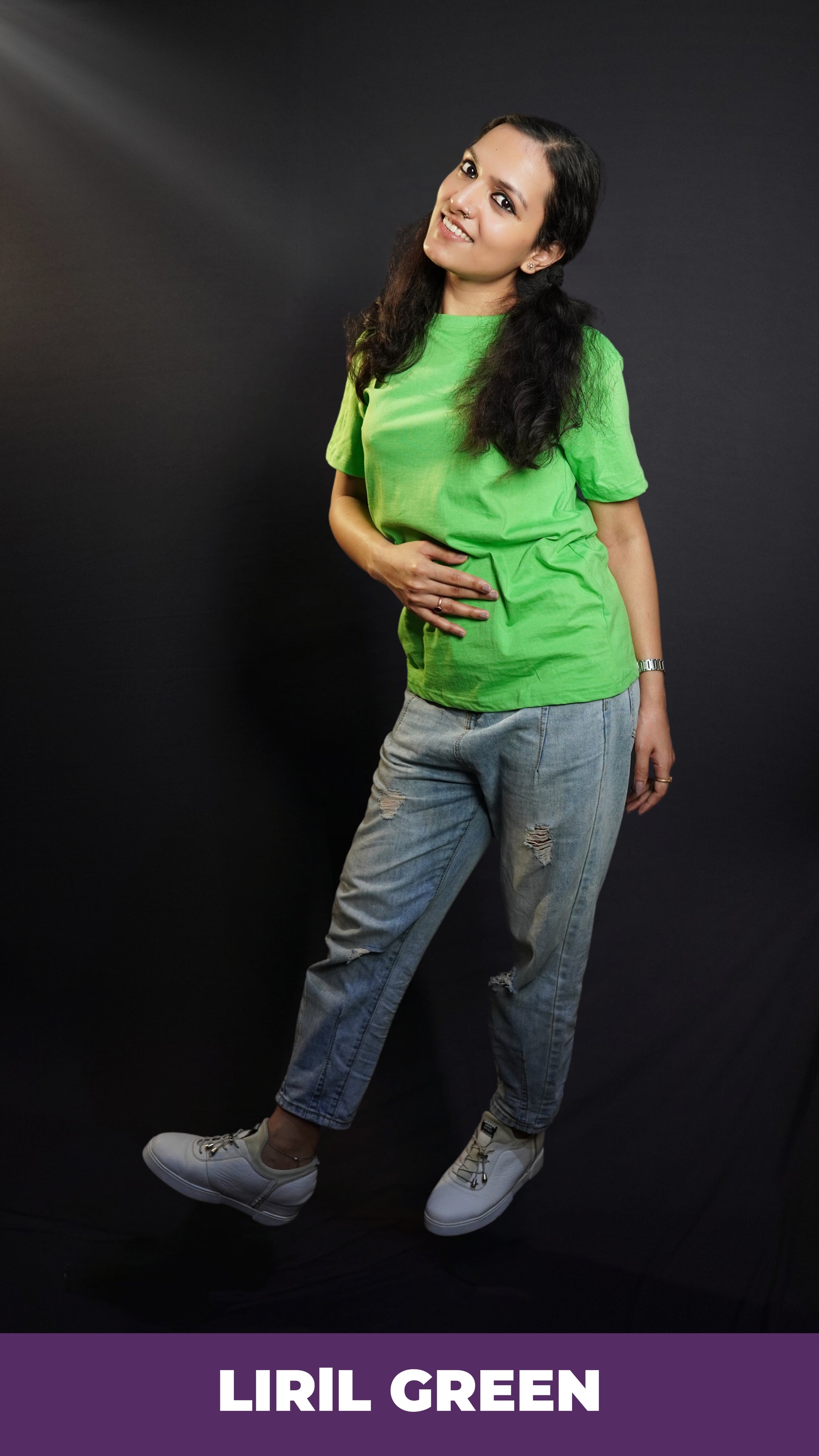 A woman in a long length unisex plain cotton liril green t-shirt, posing with her hand on her stomach and another behind her as she stands sideways, highlighting a modern comfortable fit-Muselot