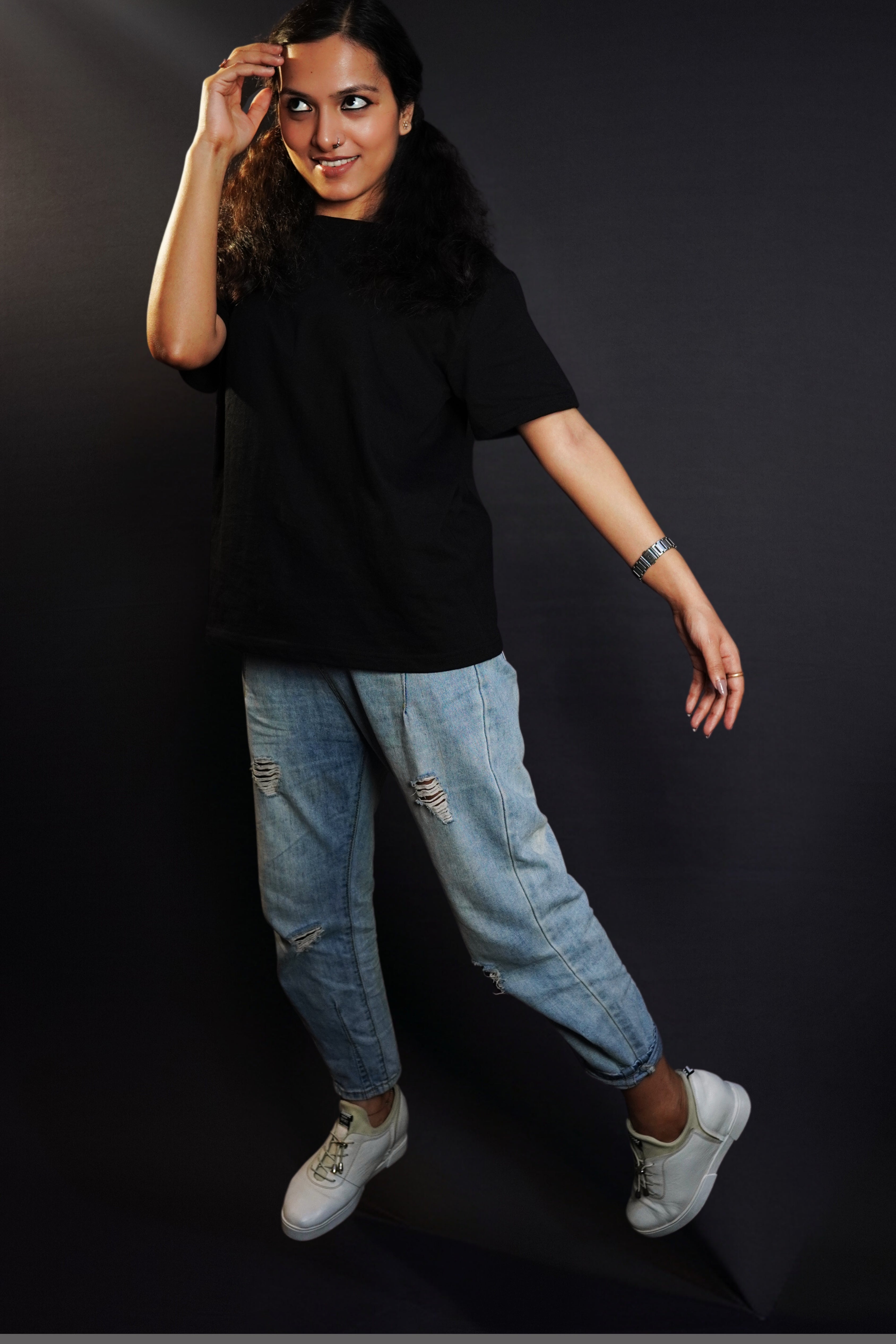 A woman posing with her hand barely touching her forehead as she sways at her side, wearing a round neck short sleeved stretchable moisture wicking midnight black t-shirt, highlighting a modern easygoing fit-Muselot