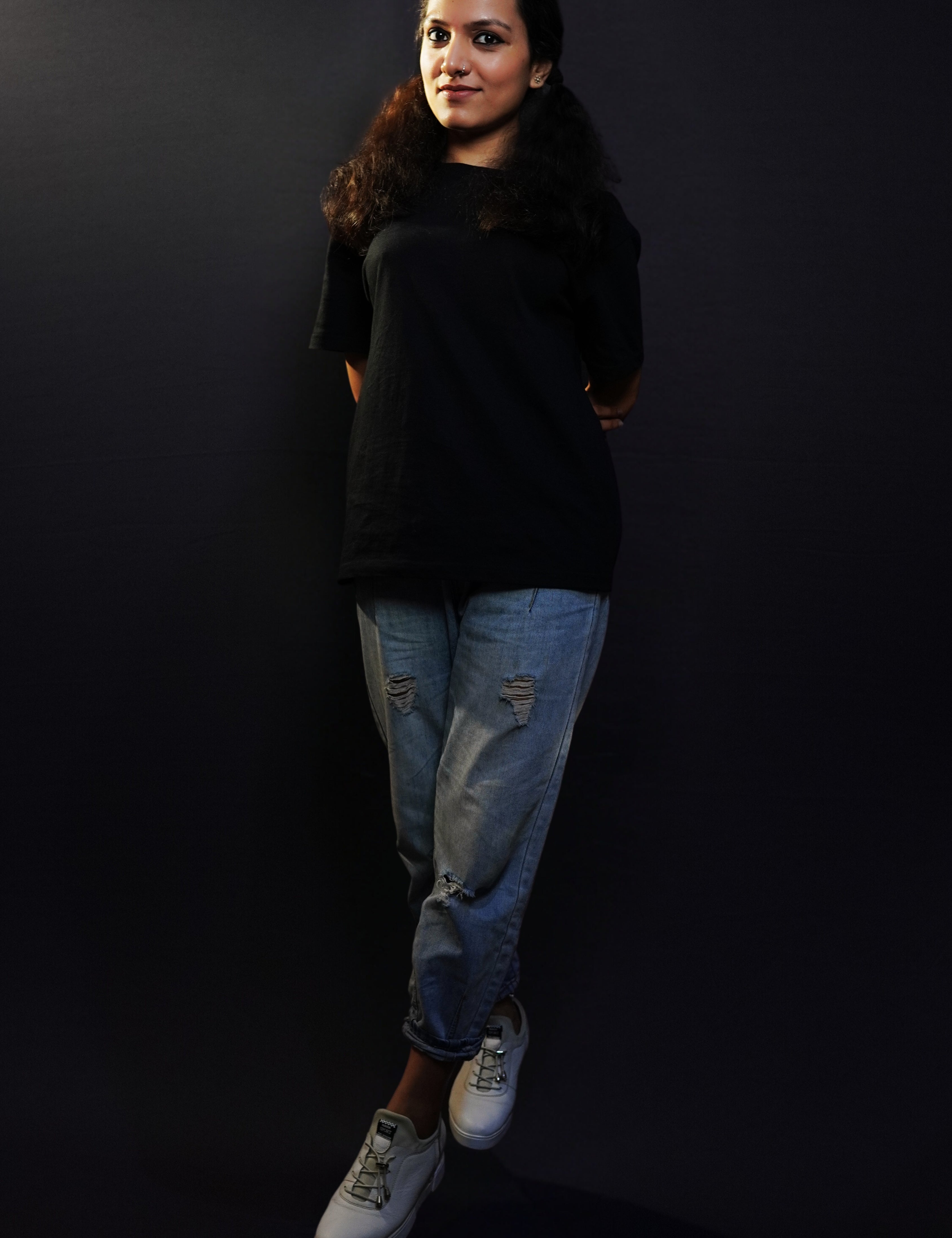 A woman posing against a dark background with her hands tied together at her back, wearing a midnight black plain plus size long length short sleeved round neck t-shirt, highlighting a classy elegant look-Muselot