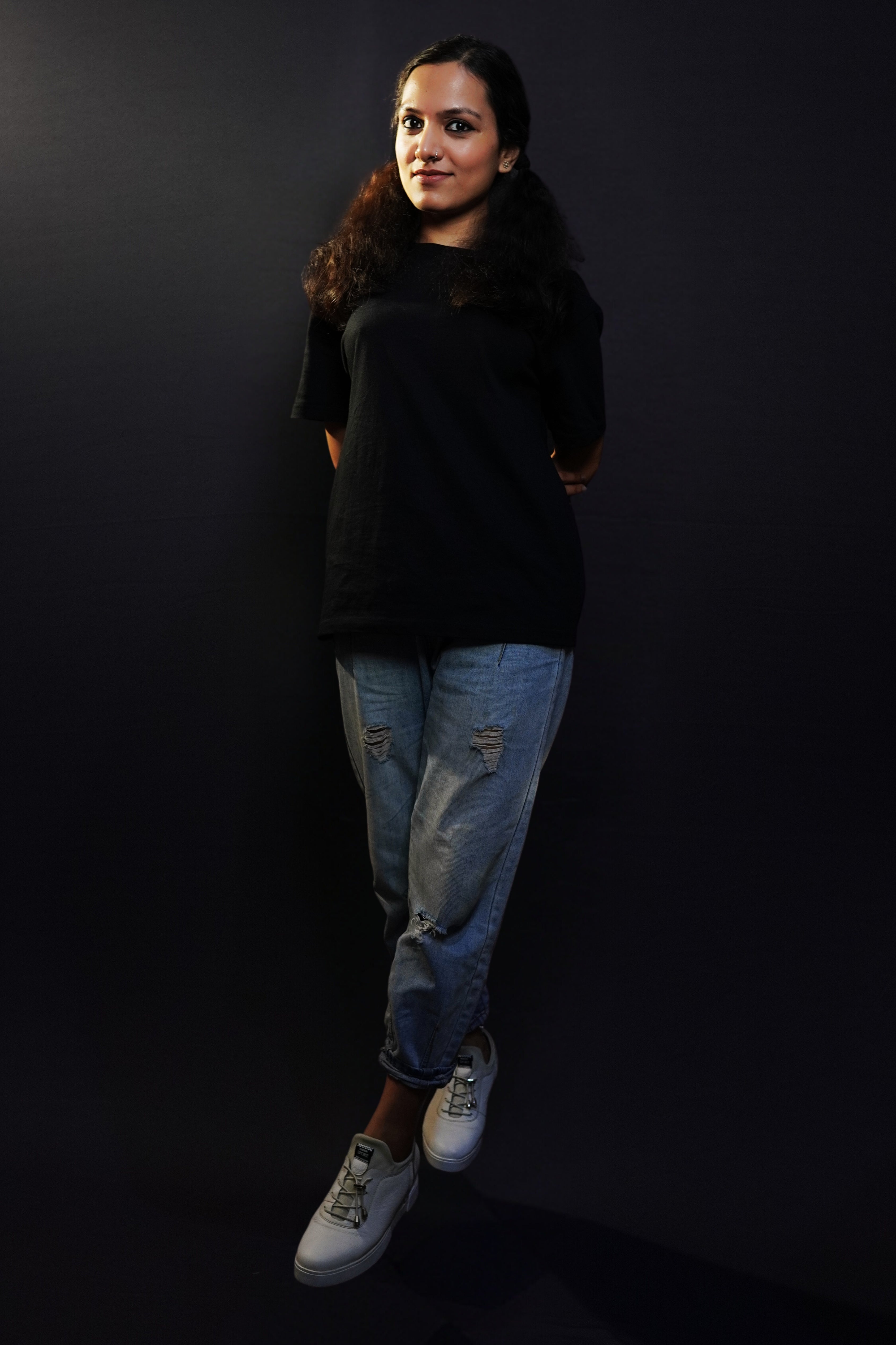 A woman posing against a dark background with her hands tied together at her back, wearing a midnight black plain plus size long length short sleeved round neck t-shirt, highlighting a classy elegant look-Muselot