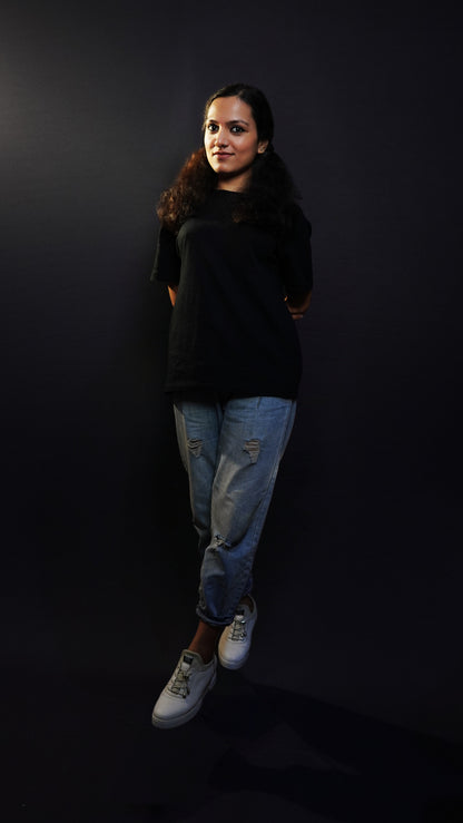 A woman posing against a dark background with her hands tied together at her back, wearing a midnight black plain plus size long length short sleeved round neck t-shirt, highlighting a classy elegant look-Muselot