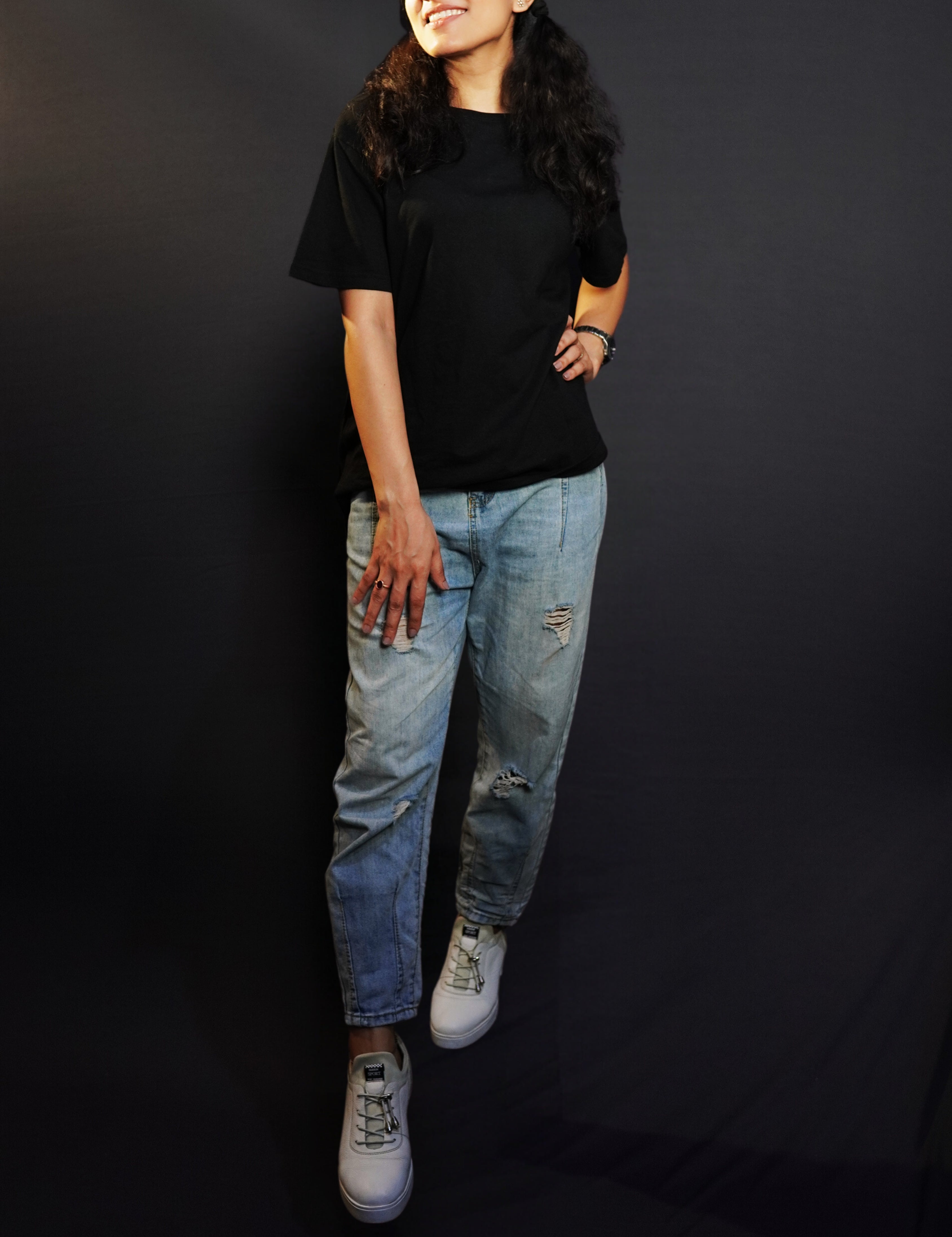 An elegant model wearing a short sleeved long length plain midnight black women's t-shirt, looking sideways as her hand gently lies on her waist and thigh, highlighting a stylish modern look-Muselot
